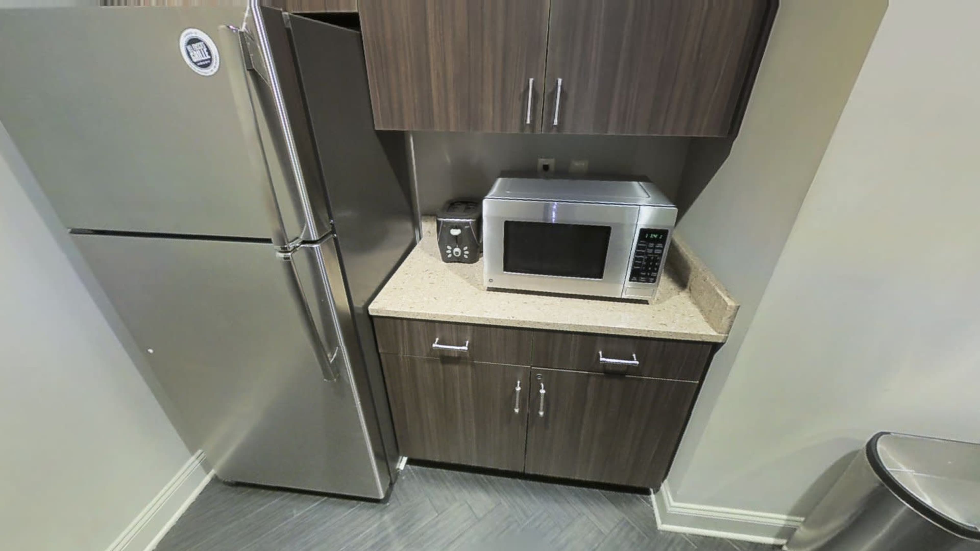 A kitchen corner with a stainless steel refrigerator next to a microwave on a countertop, below cabinets.