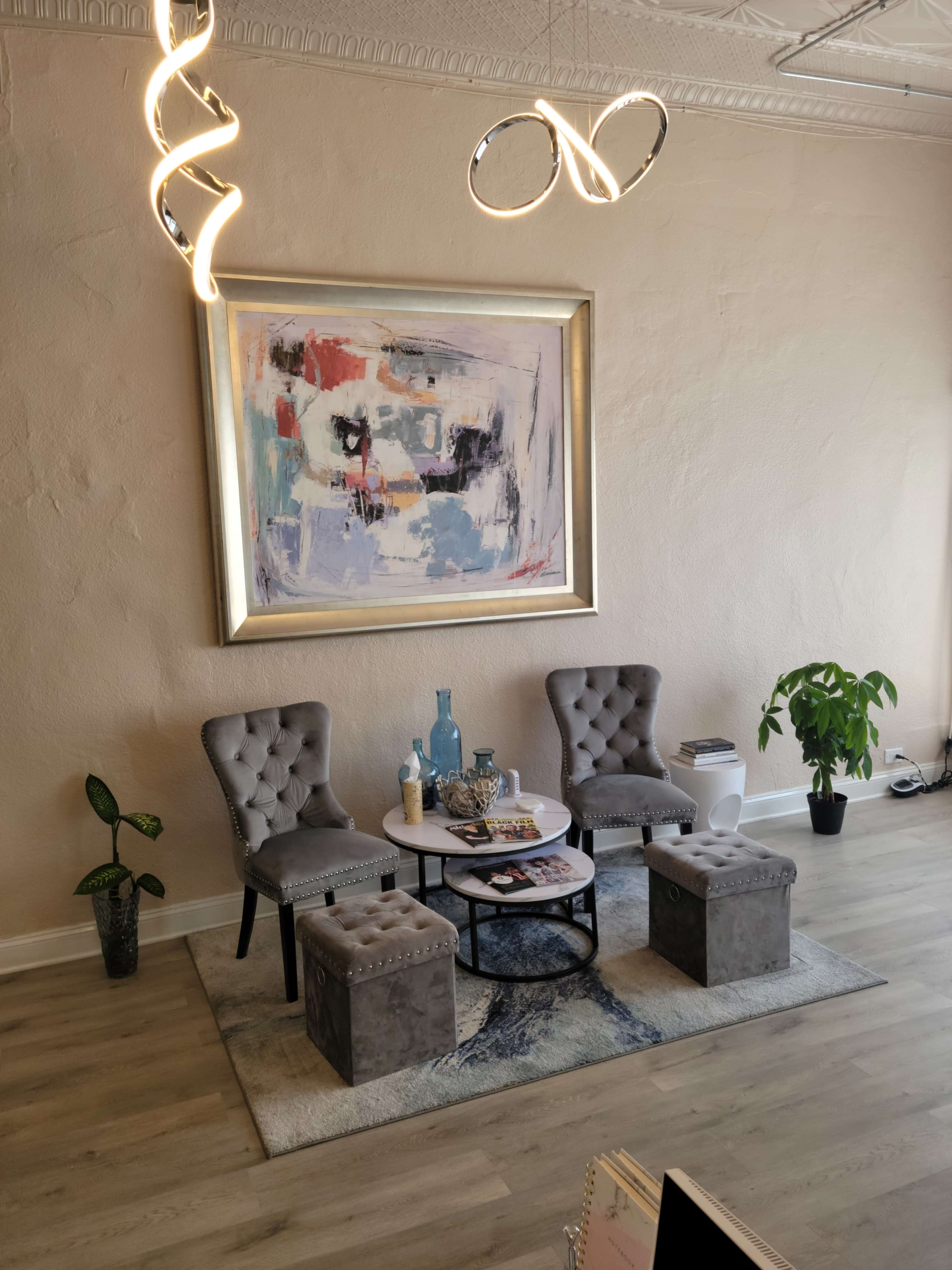 The image shows a modern interior featuring two gray tufted chairs, a round coffee table, and a decorative wall painting, all arranged on a light wood floor.