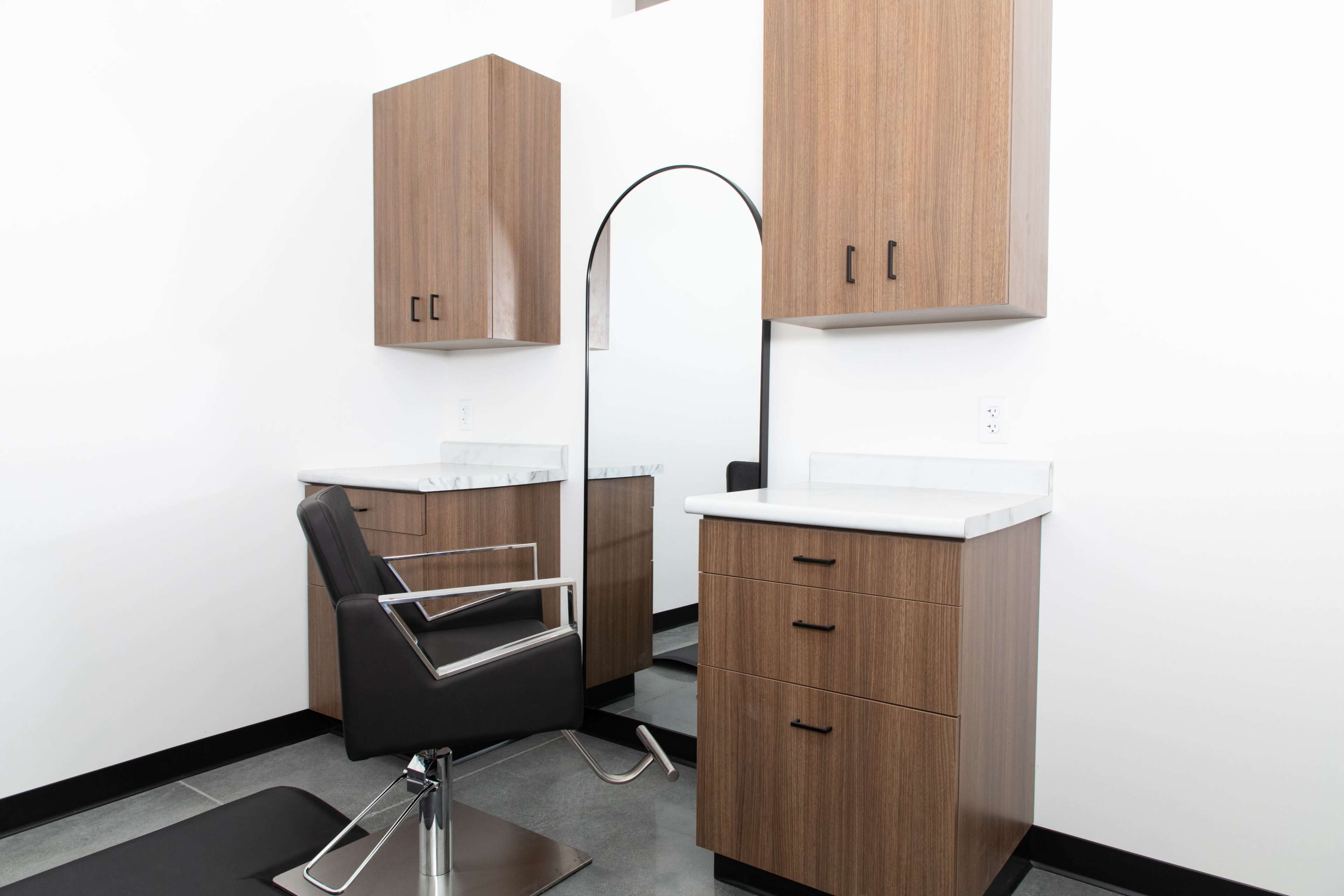 A modern hair salon interior with wooden cabinets, a mirror, and a black salon chair.
