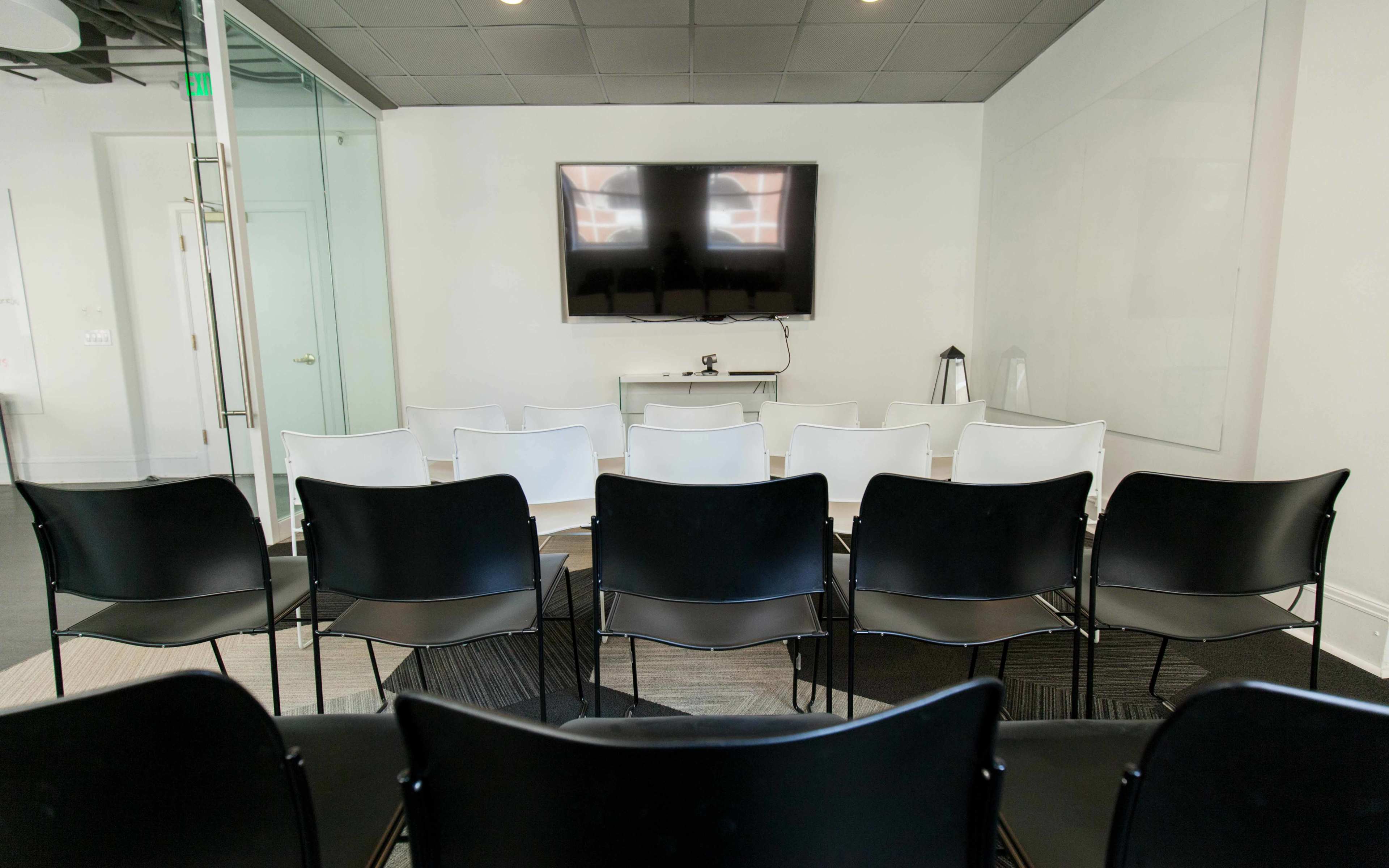 A row of black and white chairs facing a wall-mounted television in a modern conference room.