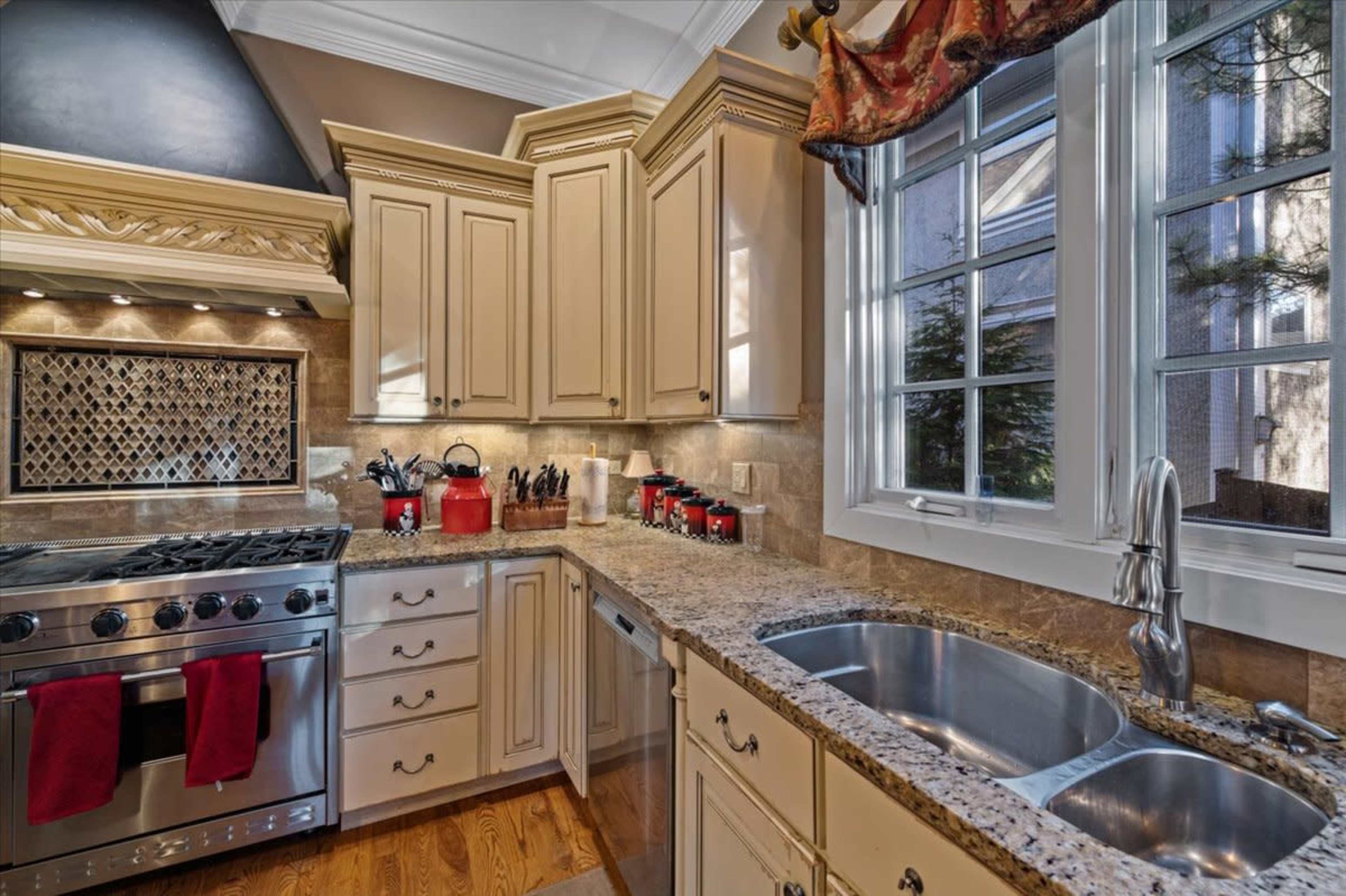 A well-organized kitchen features beige cabinets, a stainless steel stove, and a granite countertop with a double sink and large windows.