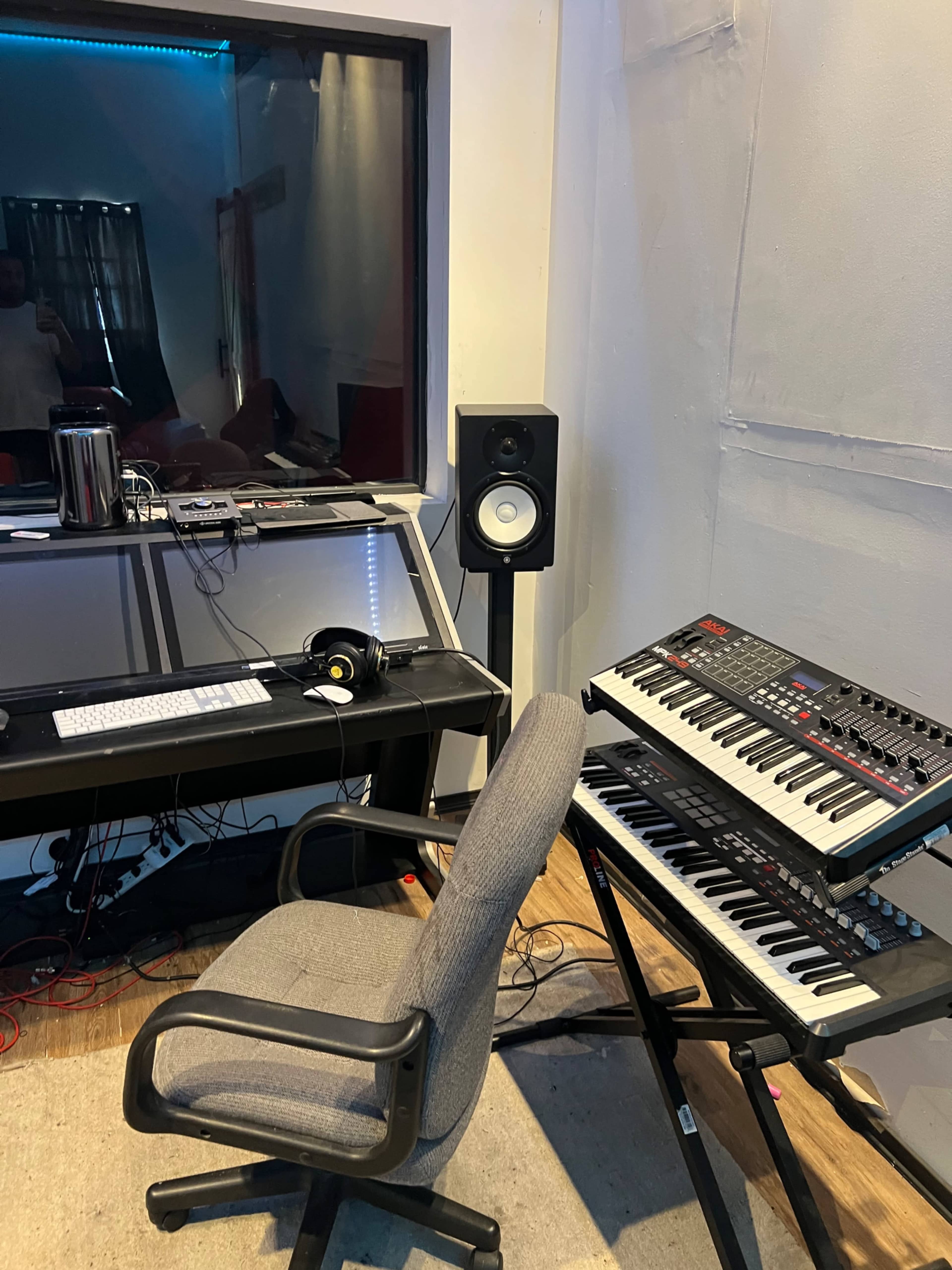 A music production studio features a computer desk, chair, audio monitors, and a synthesizer keyboard.