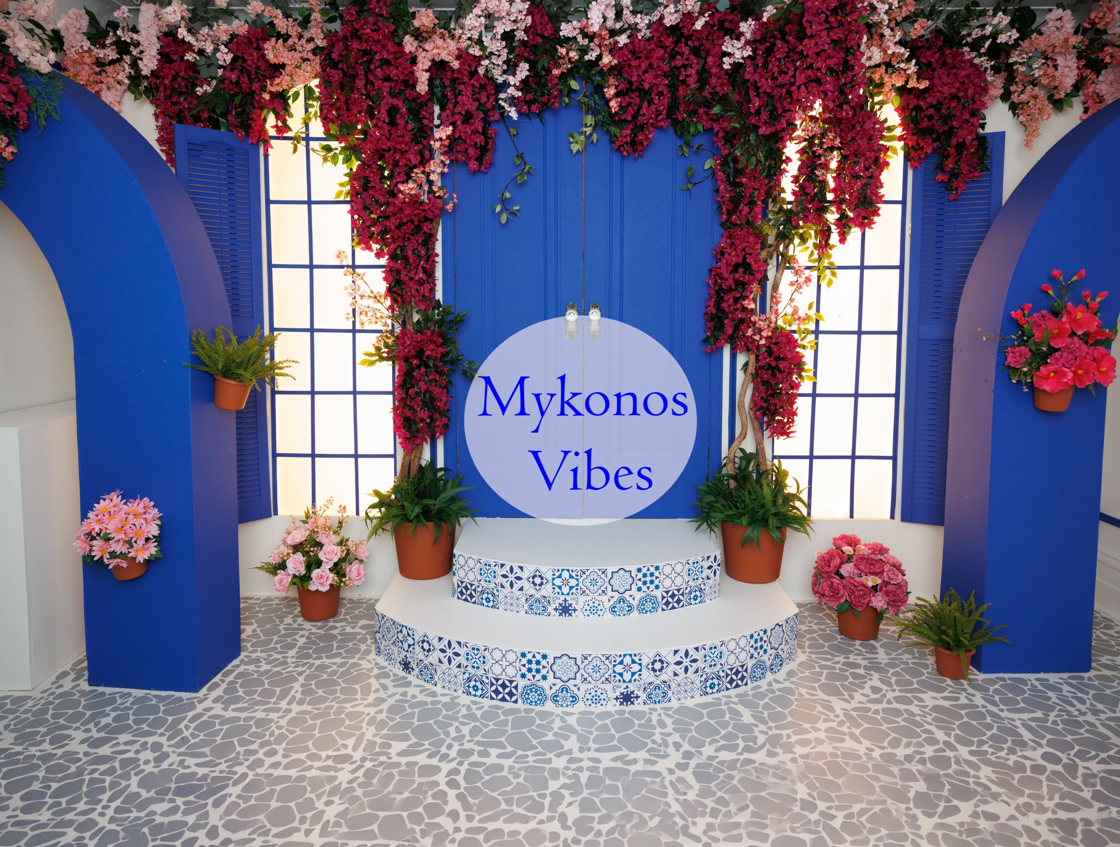 The image features a decorative setting with blue arches, vibrant pink and red flowers, and potted plants, evoking a Mediterranean aesthetic.