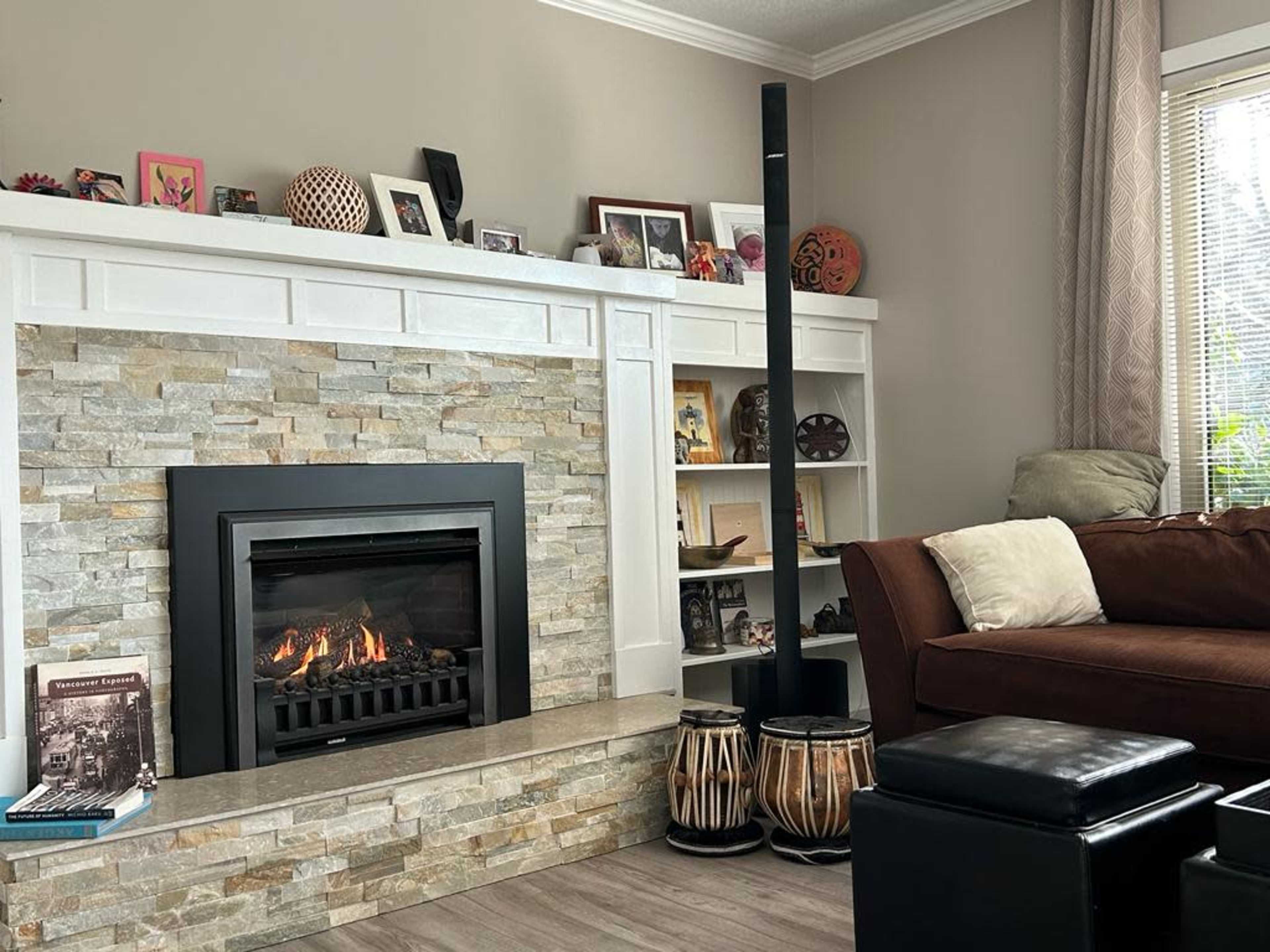 The image shows a modern living room with a stone fireplace, a dark sofa, a tall black speaker, and decorative items on the shelves and mantel.