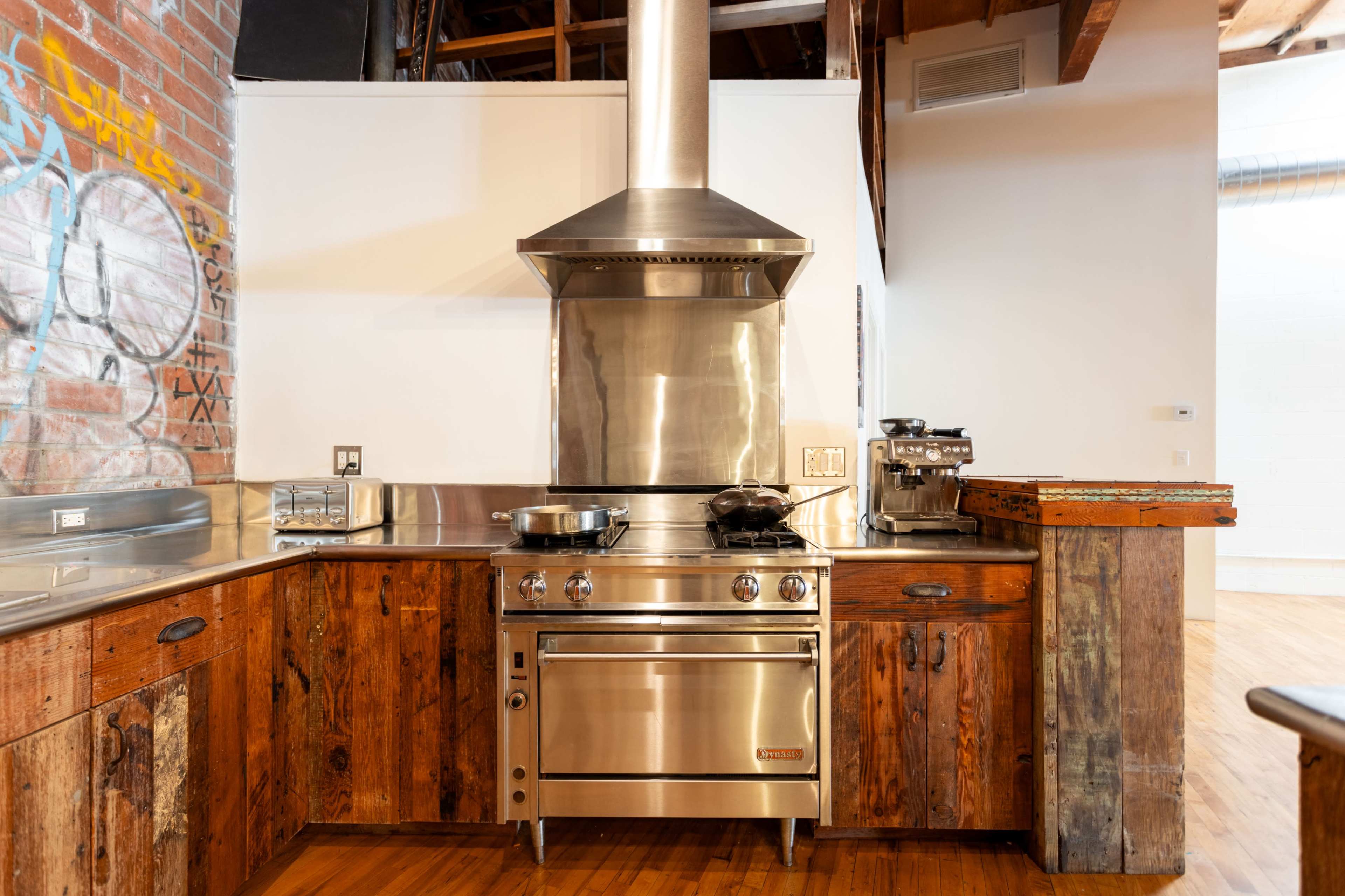 A modern kitchen with stainless steel appliances, a hood over a gas stove, and rustic wooden cabinetry.