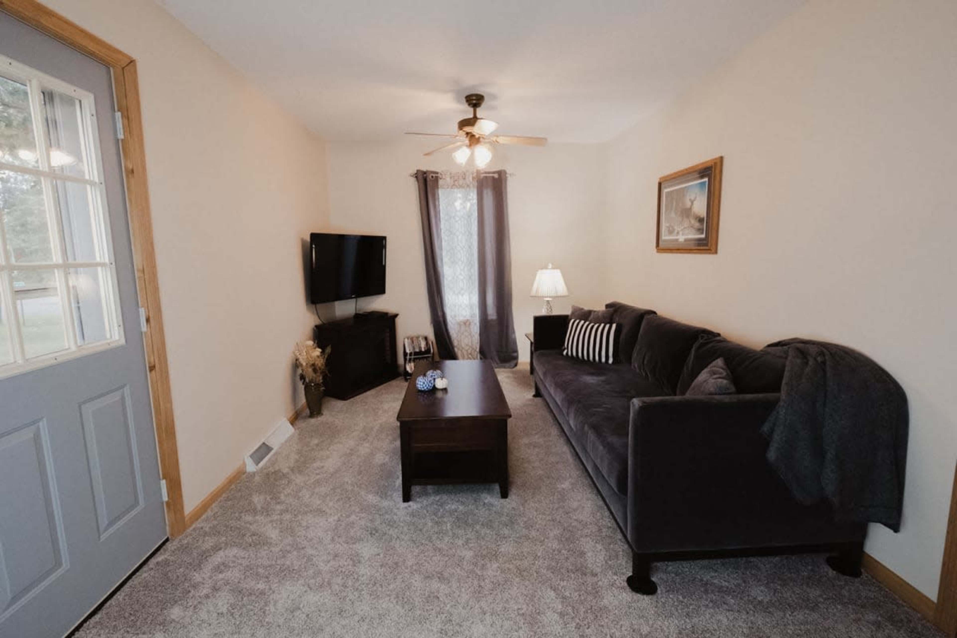 A cozy living room featuring a gray sofa, a wooden coffee table, a television, and a door leading outside.