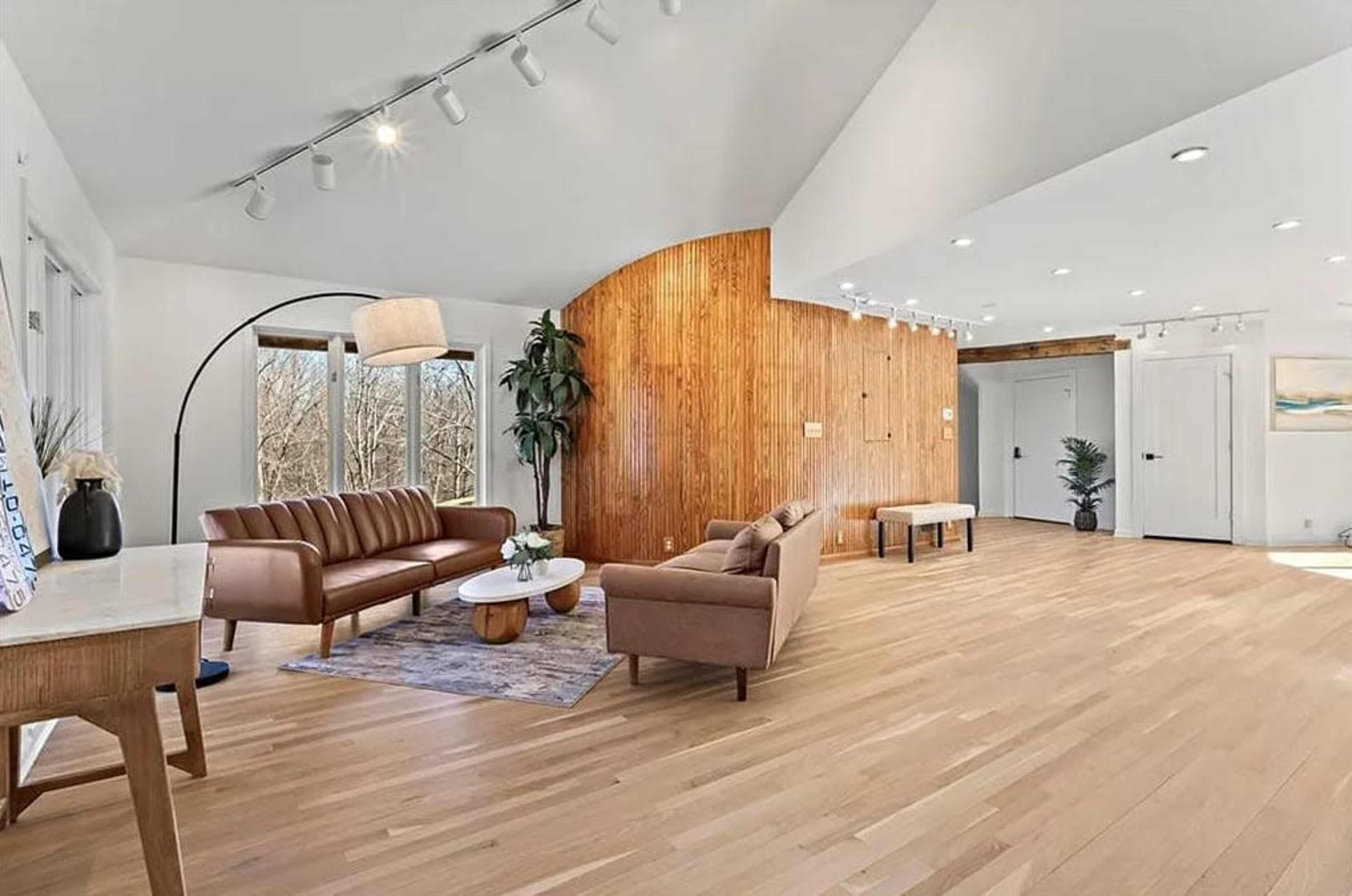 The image shows a modern living room with hardwood floors, a curved wooden accent wall, and sleek furniture arranged around a coffee table.