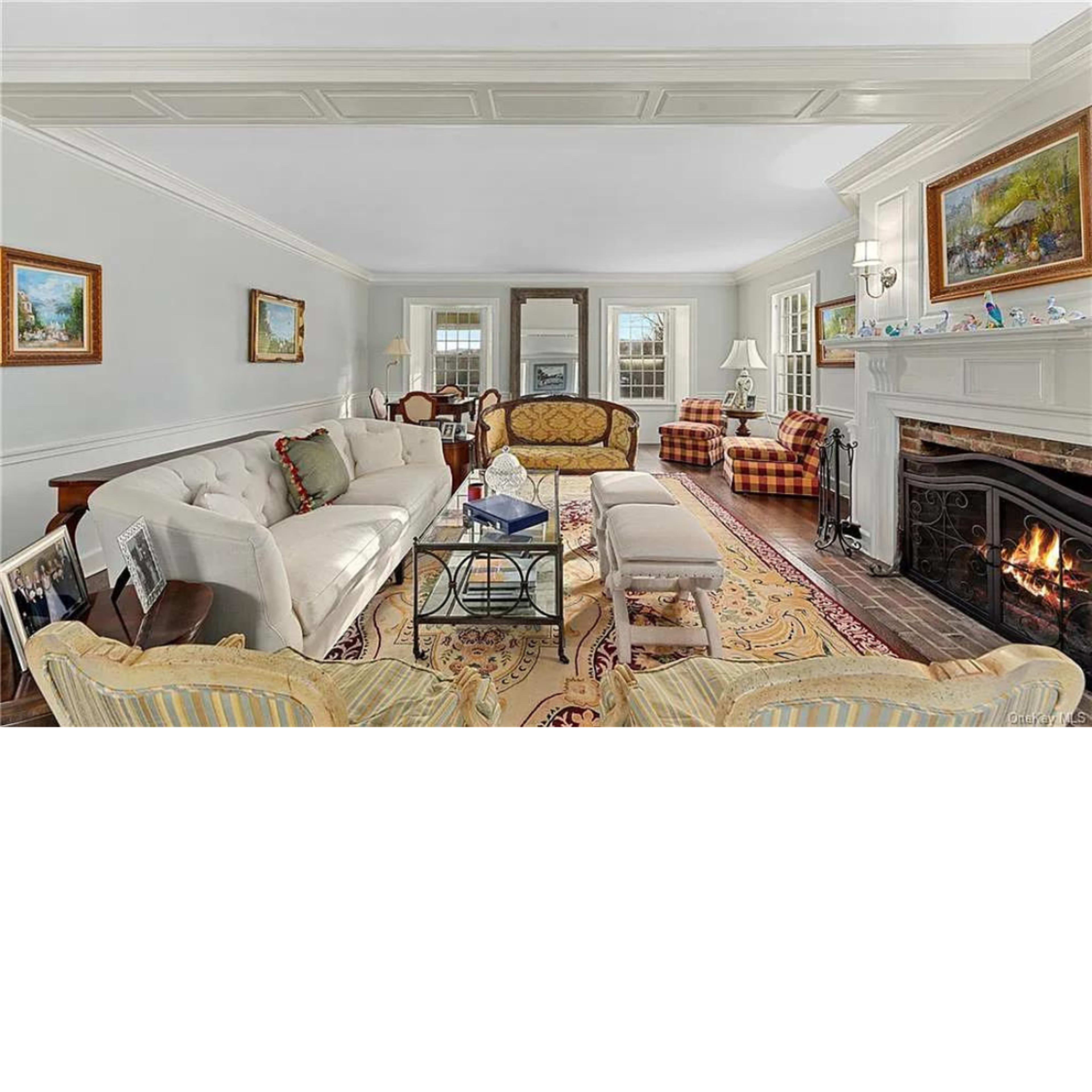 The living room features a beige sofa, patterned armchairs, and a fireplace, all arranged around a central area rug under soft natural light.