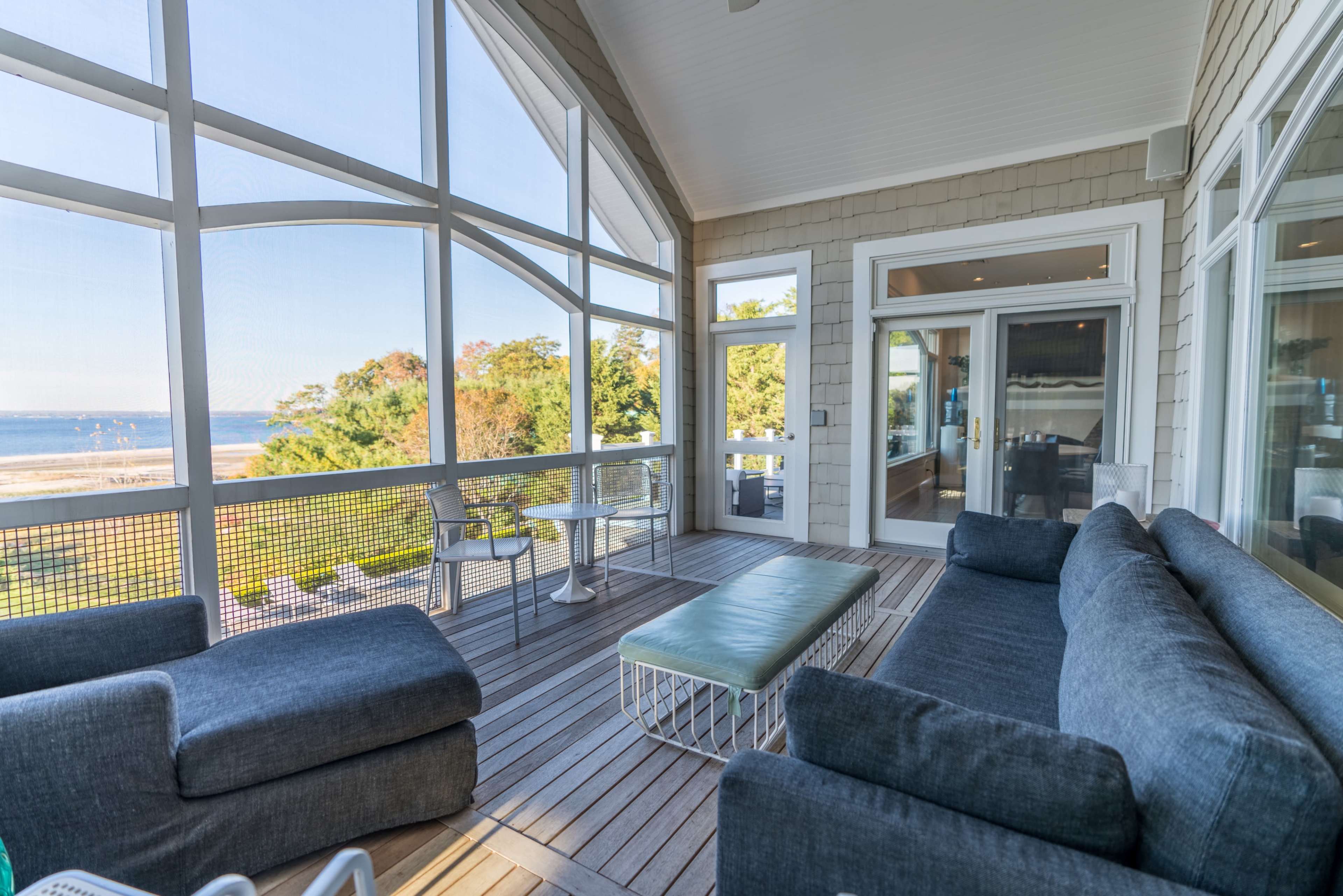 A modern outdoor seating area features a sectional sofa and a coffee table, overlooking a scenic view of the water and trees.