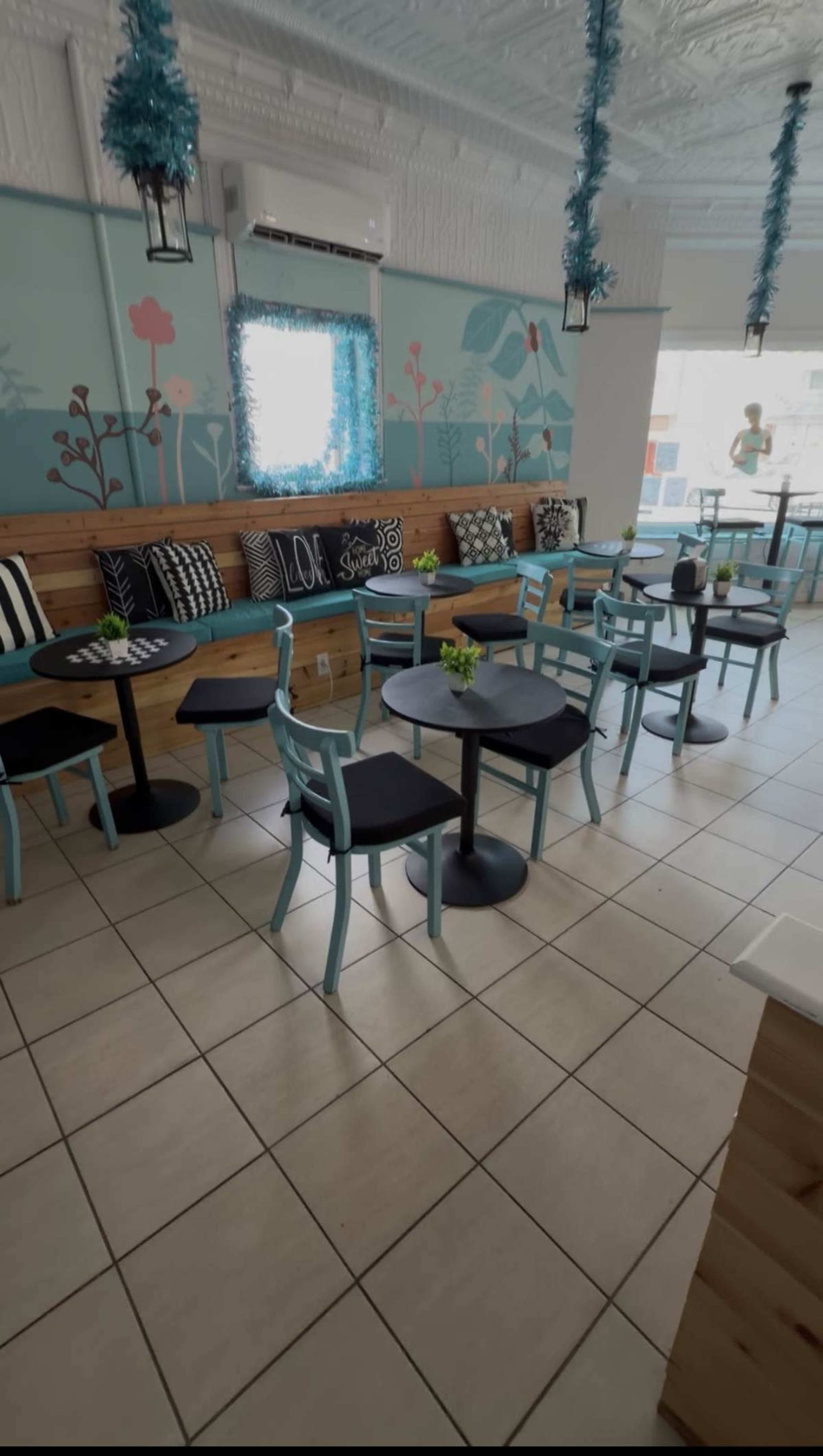 The image shows a brightly decorated café with turquoise chairs, wooden seating, and tables arranged in a clean, tidy space.