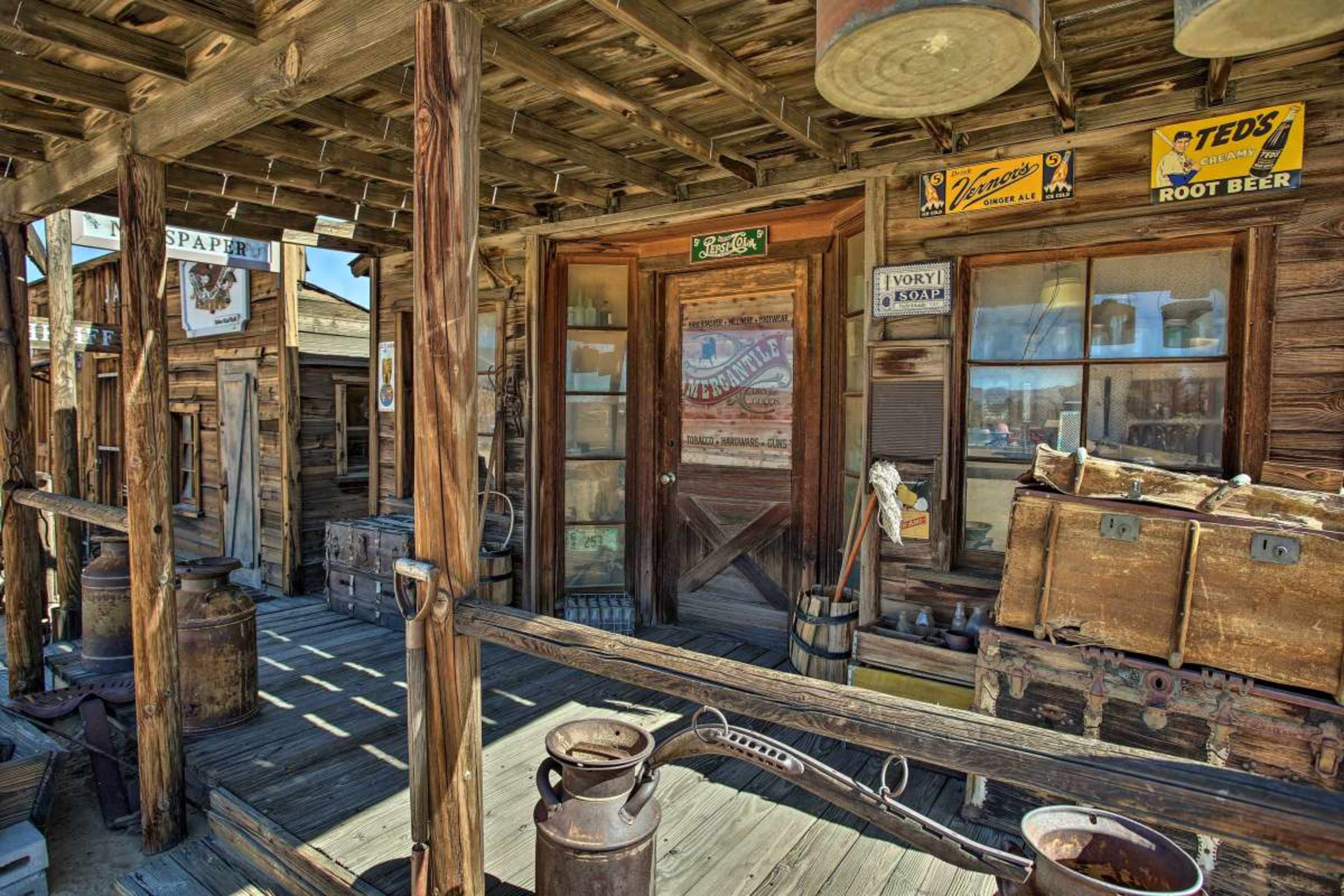 A weathered wooden storefront with a porch, featuring vintage signs and old-fashioned containers.