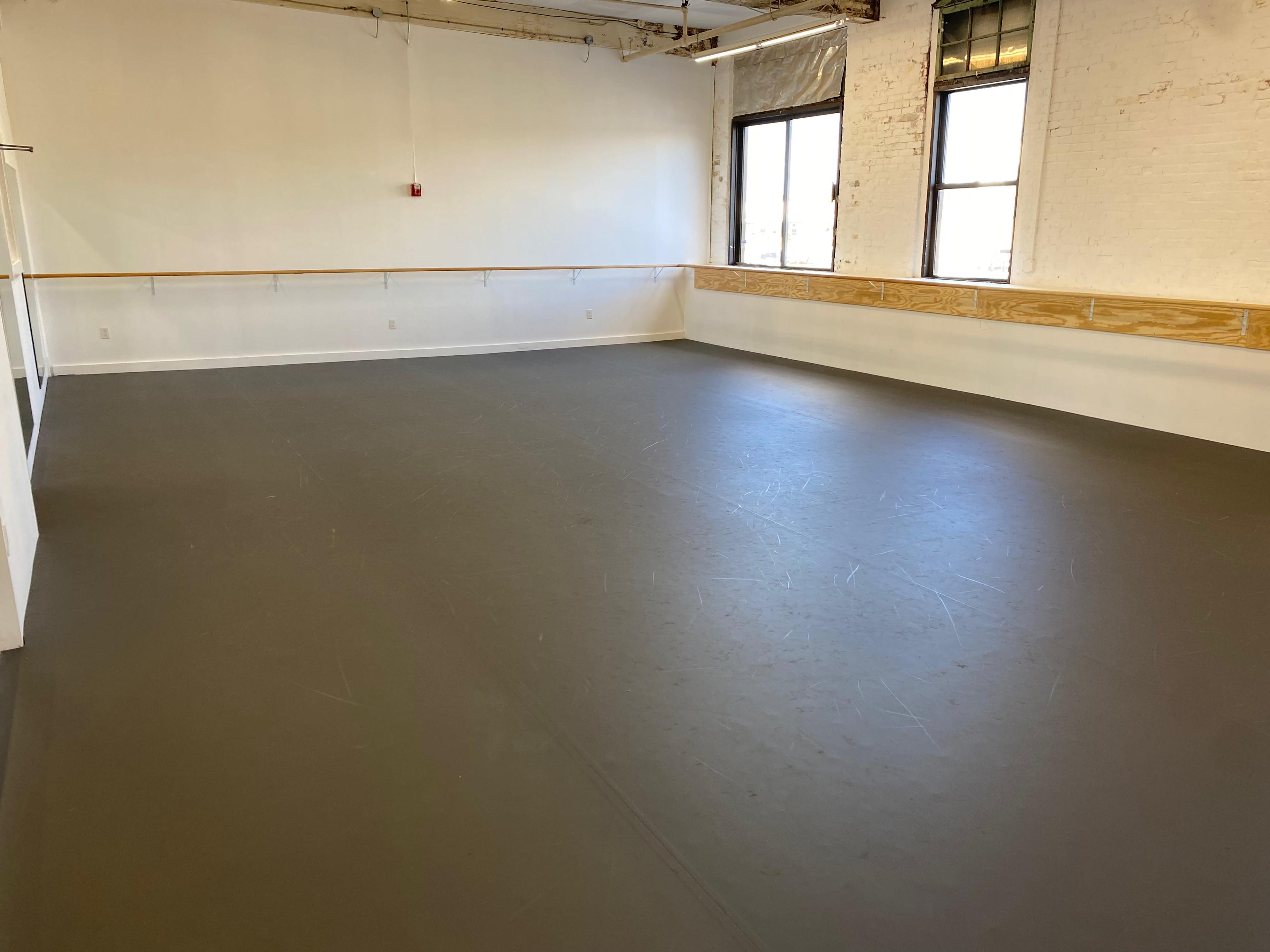 An empty dance studio with a smooth gray floor and large windows.