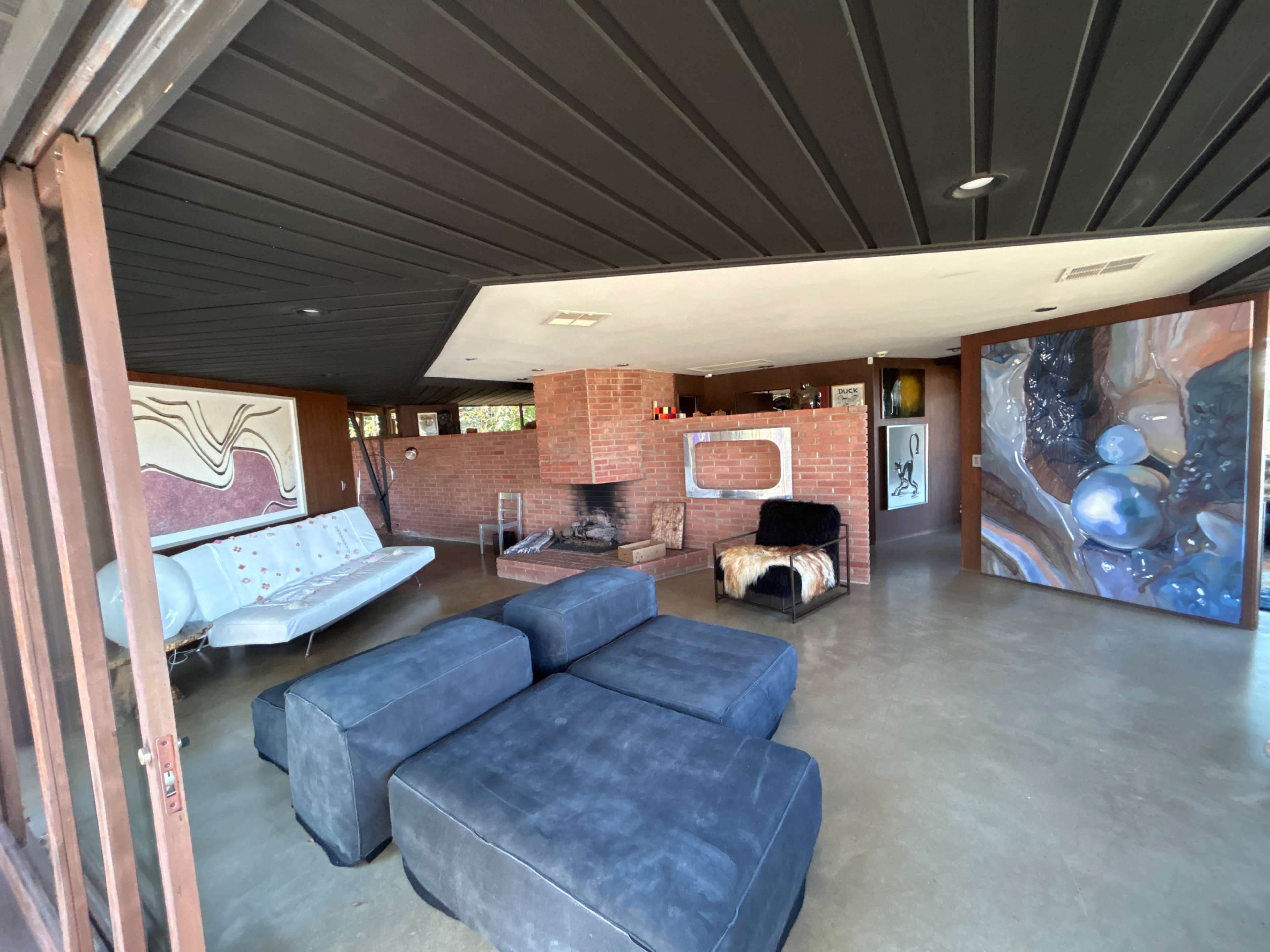 A modern living room with a mix of brick and concrete walls, featuring a sectional sofa, a fireplace, and large artwork on the walls.