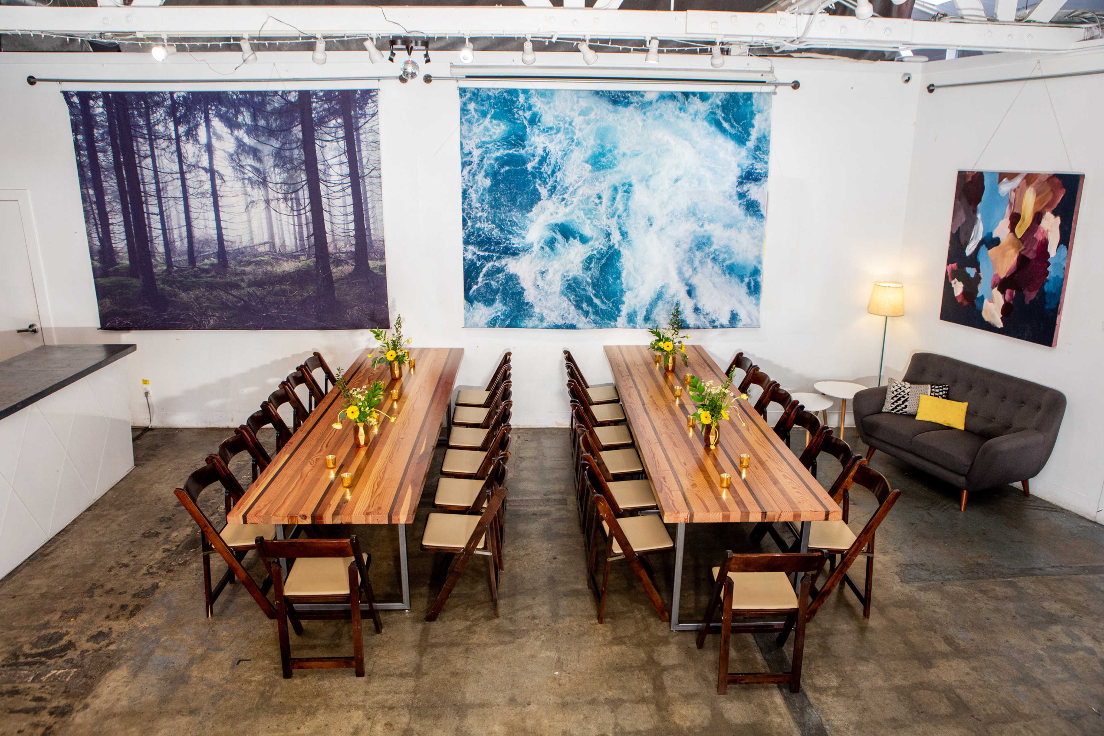 A spacious dining area features two large tables arranged in a U-shape, with floral centerpieces and artwork of a forest and ocean on the walls.