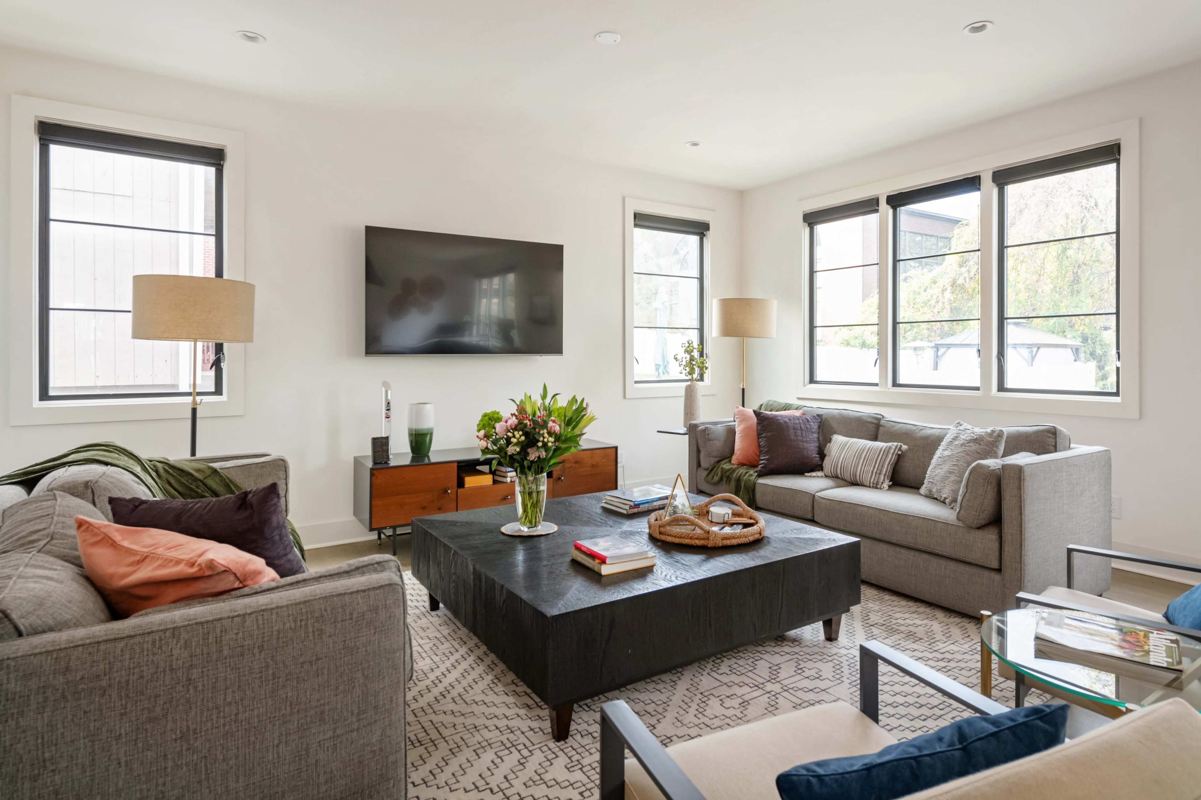 The image shows a modern living room featuring two sofas, a coffee table, a television mounted on the wall, and several decorative elements.