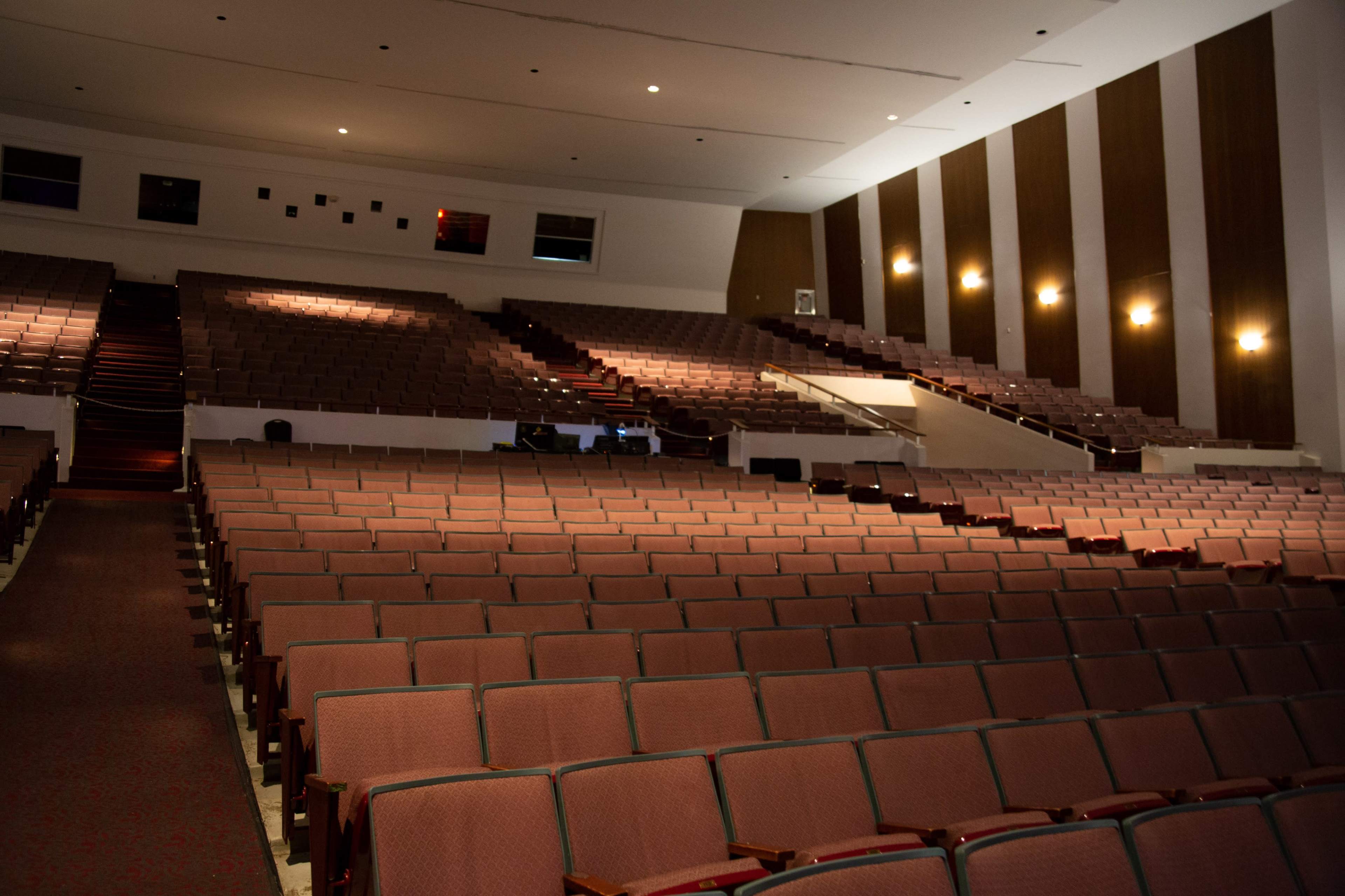 An empty auditorium with rows of brown seats arranged in a steeply tiered layout.