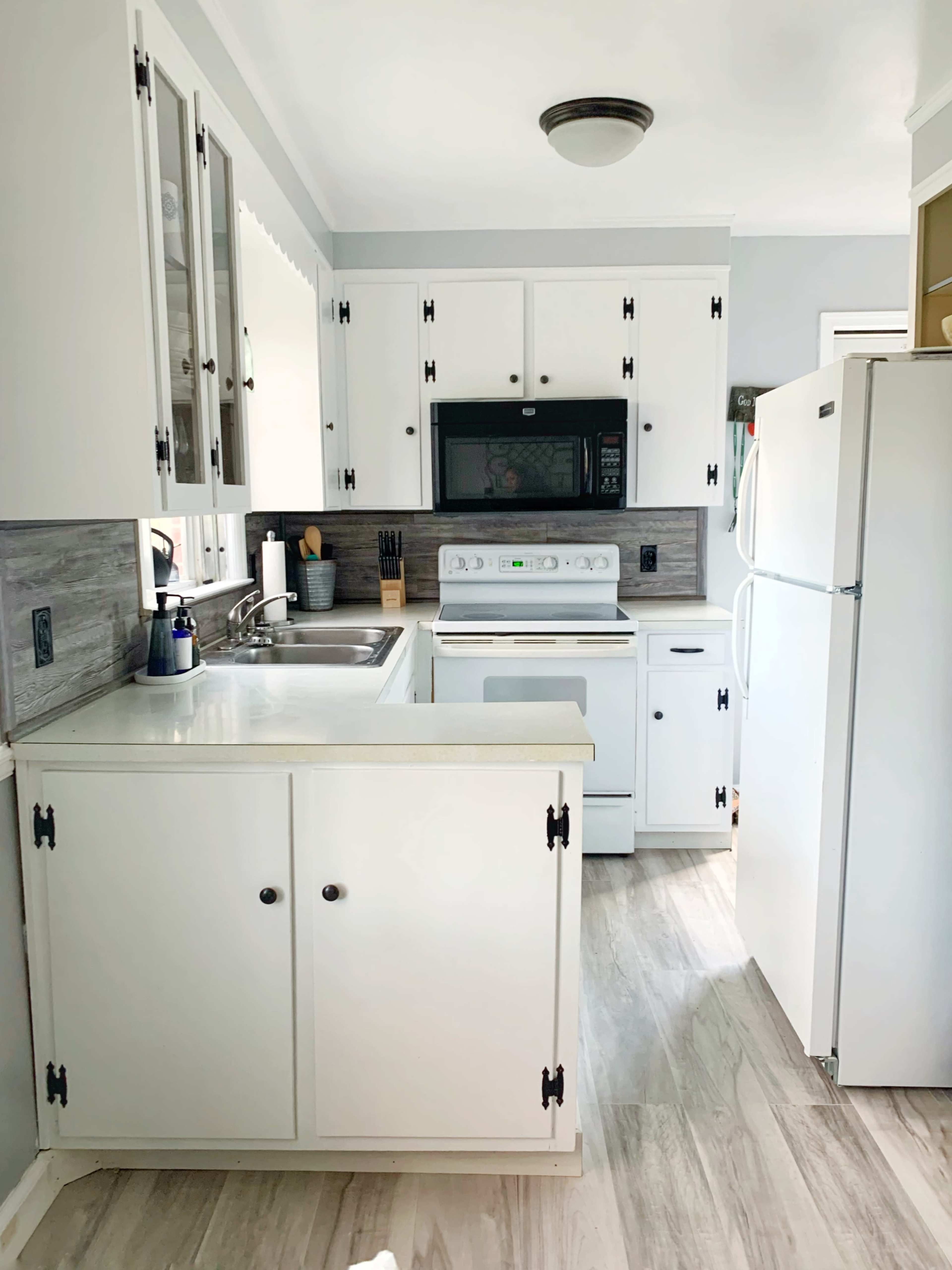 A small kitchen features white cabinets, a sink, a microwave, an oven, and a refrigerator.