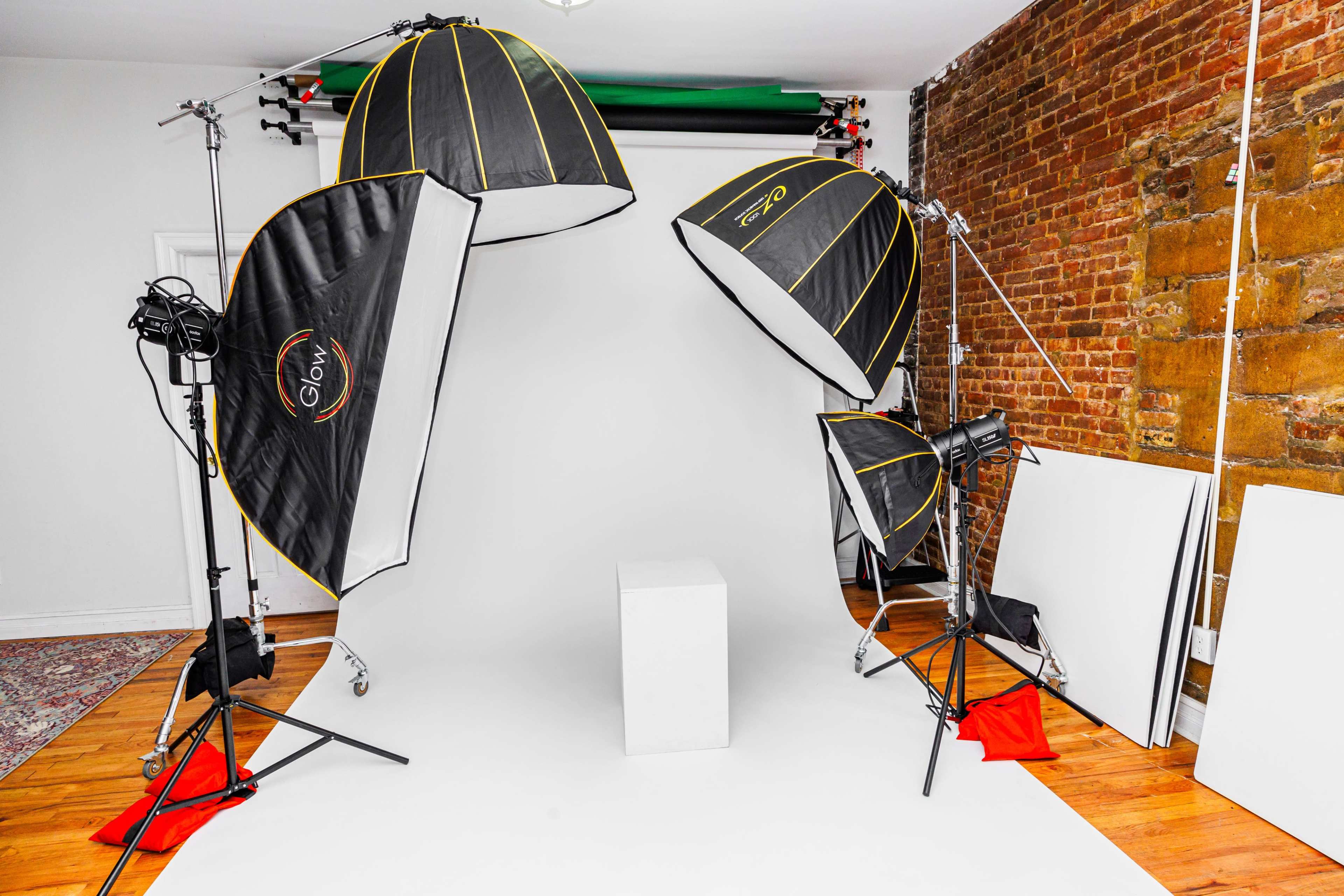 A photography studio with three large softbox lights positioned around a white backdrop and an empty square pedestal in the center.
