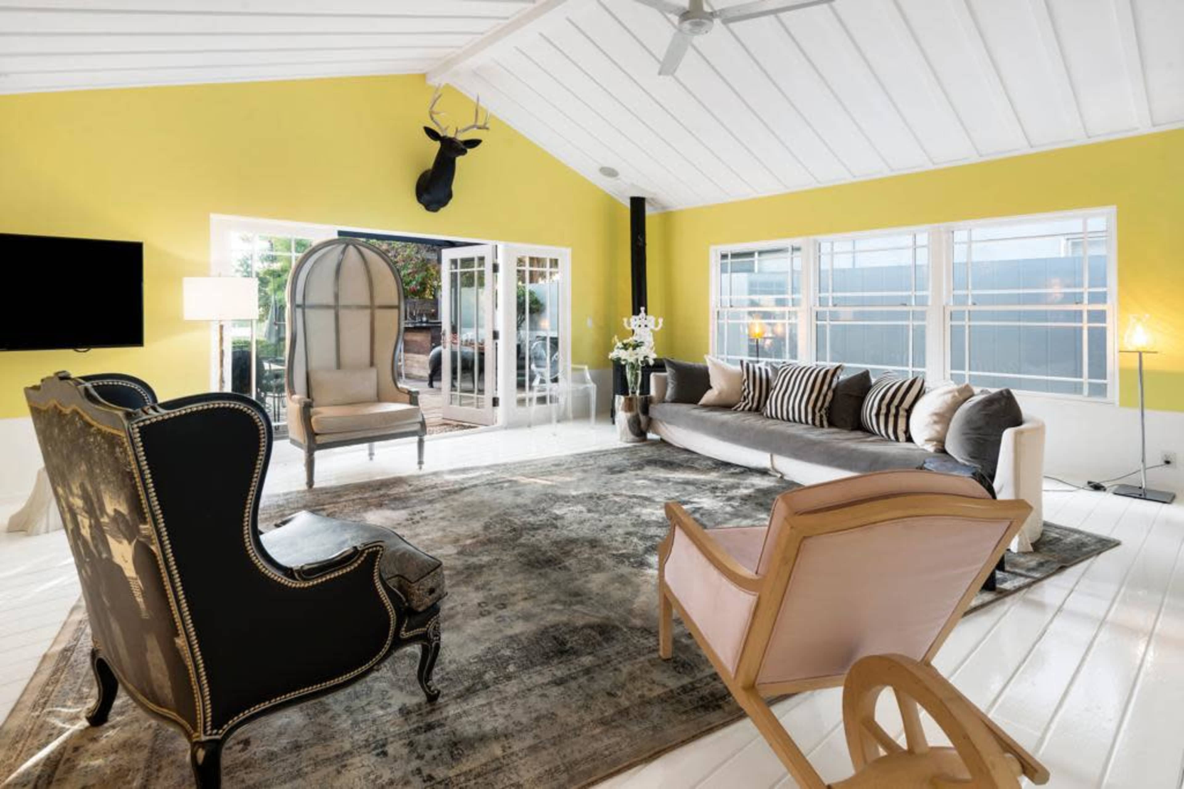The room features a bright yellow wall, contemporary furniture, a large area rug, and large windows allowing natural light to fill the space.