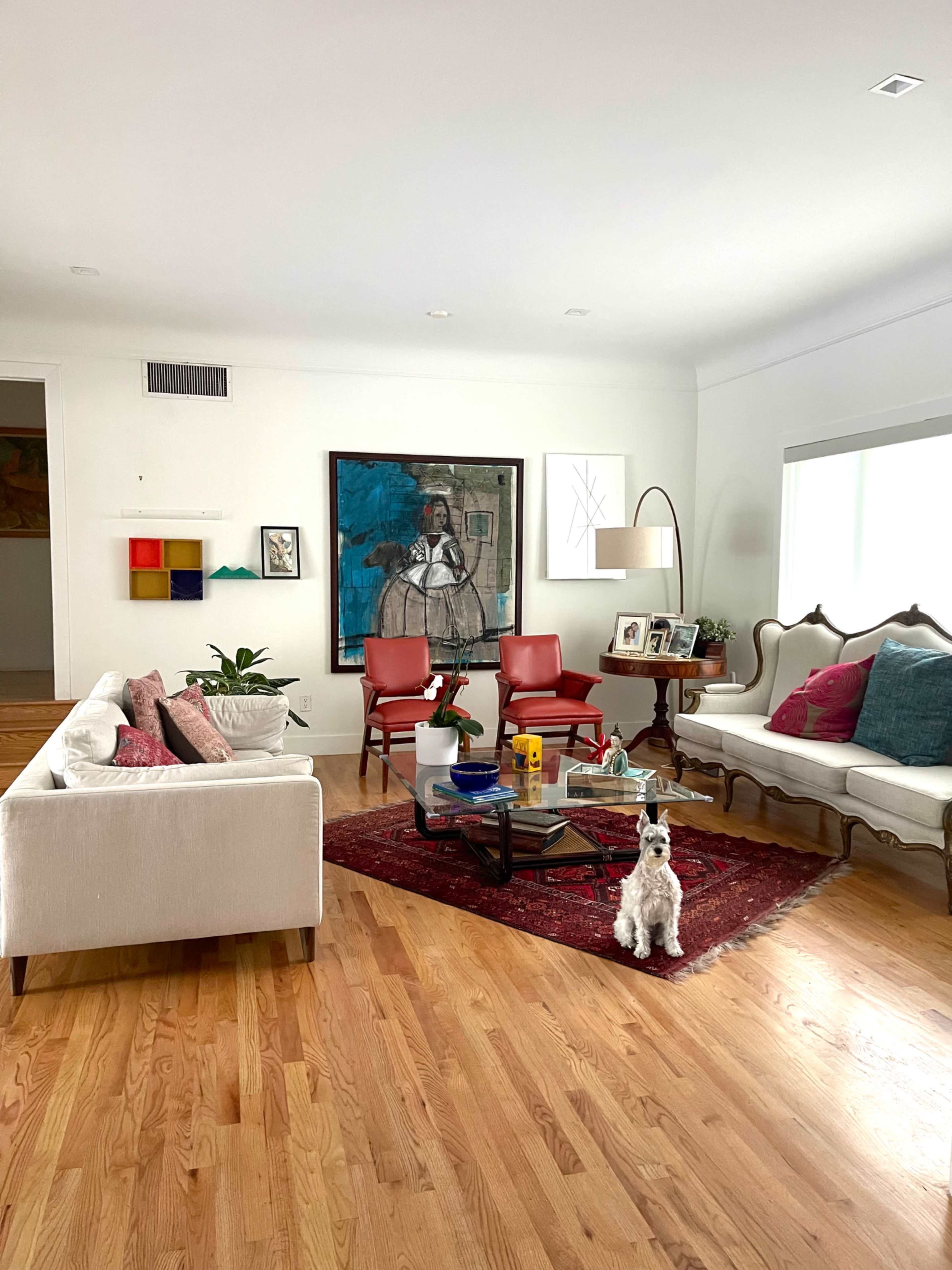 A cozy living room features a mix of modern and traditional furniture, a large painting on the wall, and a small dog sitting on a rug.