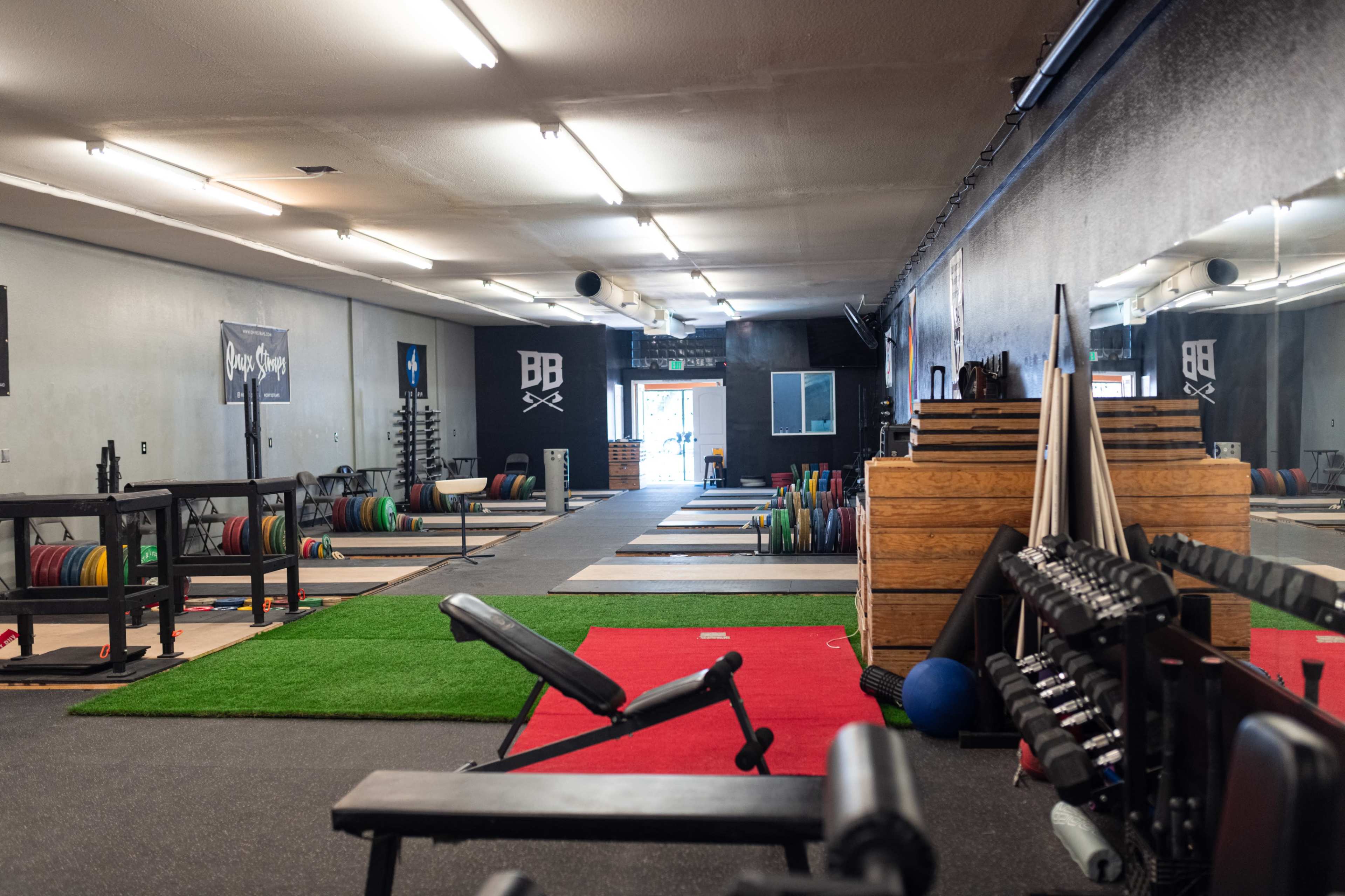 A spacious gym with weightlifting equipment, benches, and a variety of colorful plates arranged on racks along with a section of turf flooring.