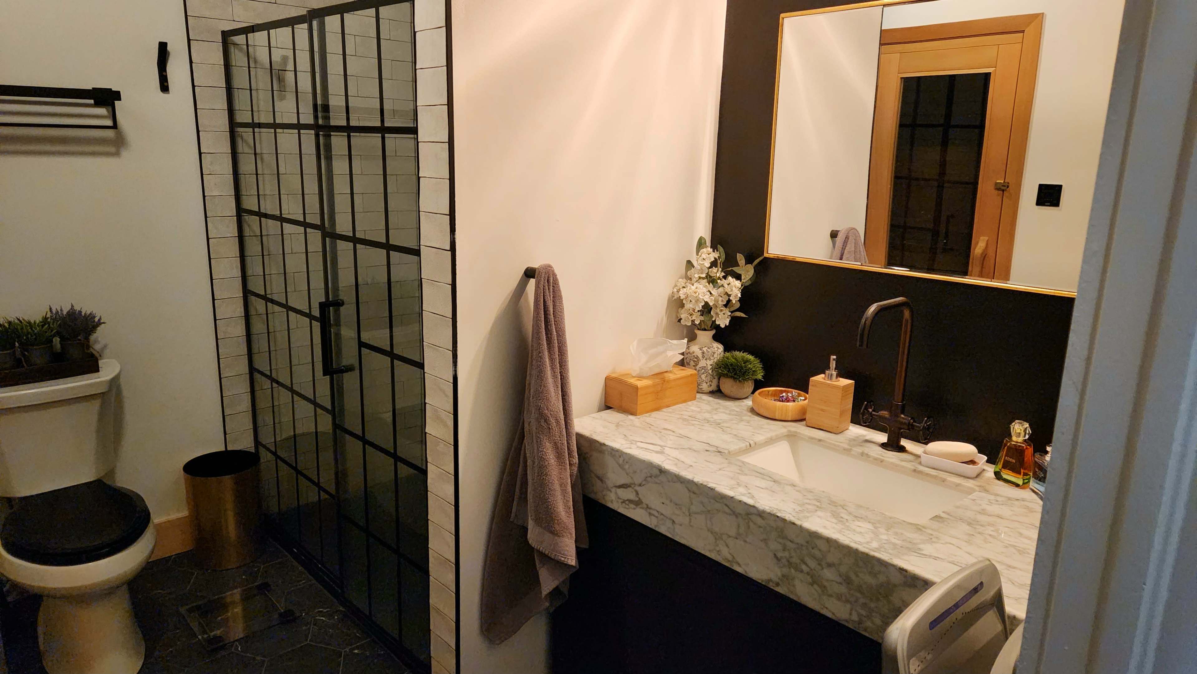 A modern bathroom with a marble countertop, a sink, a wall-mounted mirror, a glass shower enclosure, and a toilet in the corner.