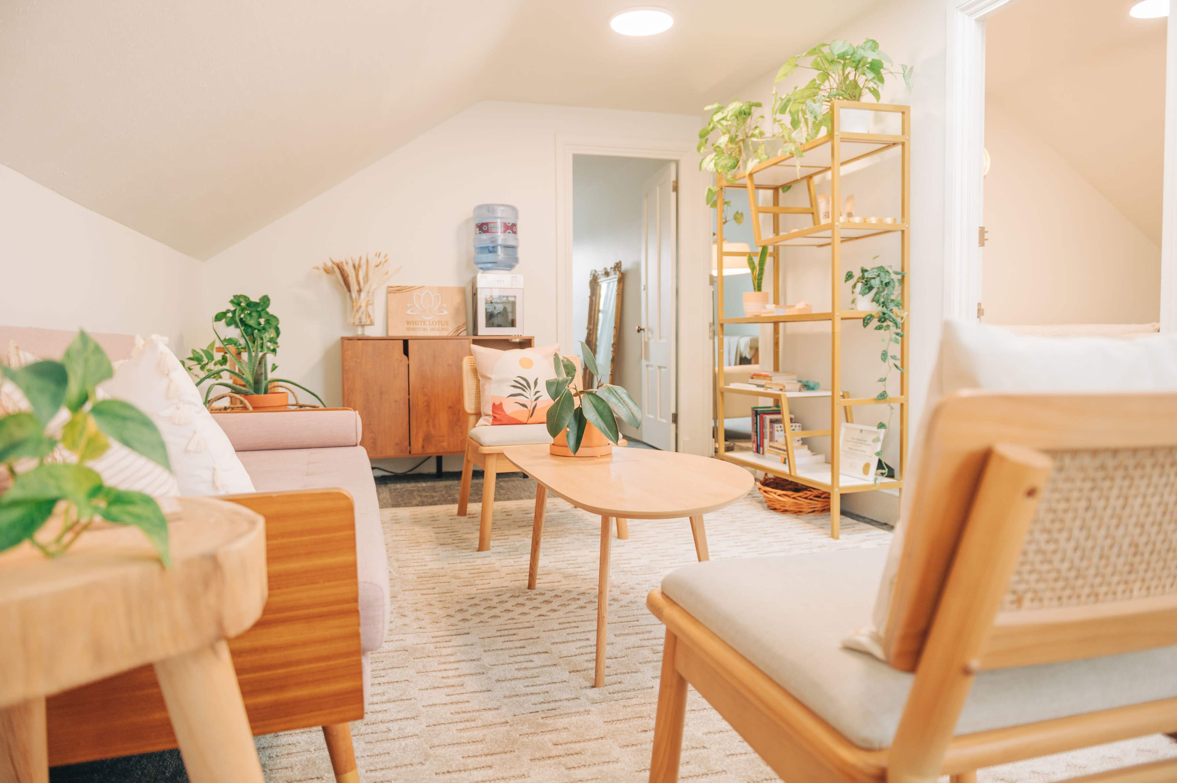 A cozy attic living space featuring two chairs, a wooden table, a sofa, and shelves adorned with plants and decorative items.