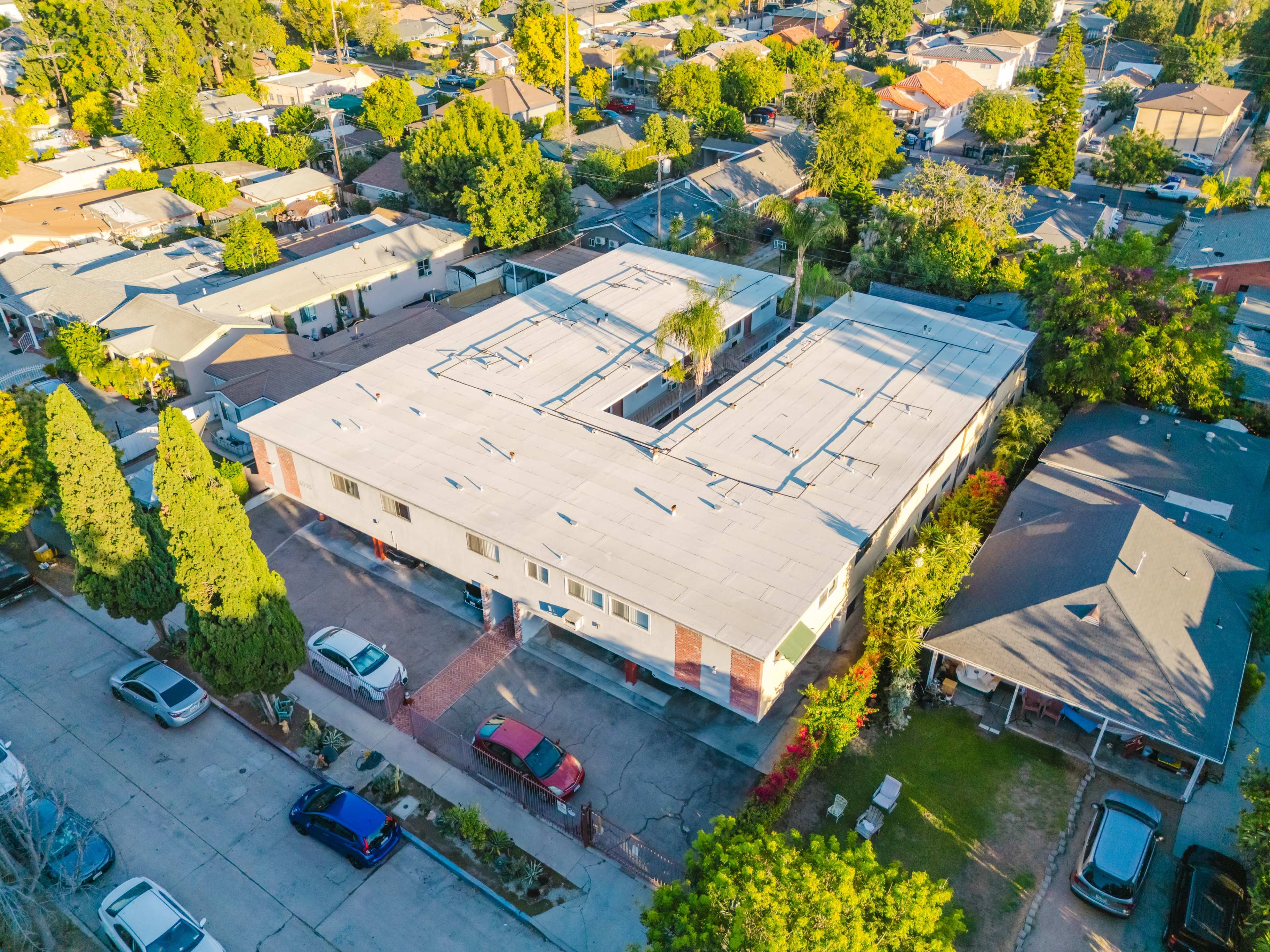 The image shows an aerial view of a residential area featuring a flat-roofed building surrounded by trees and several nearby houses.