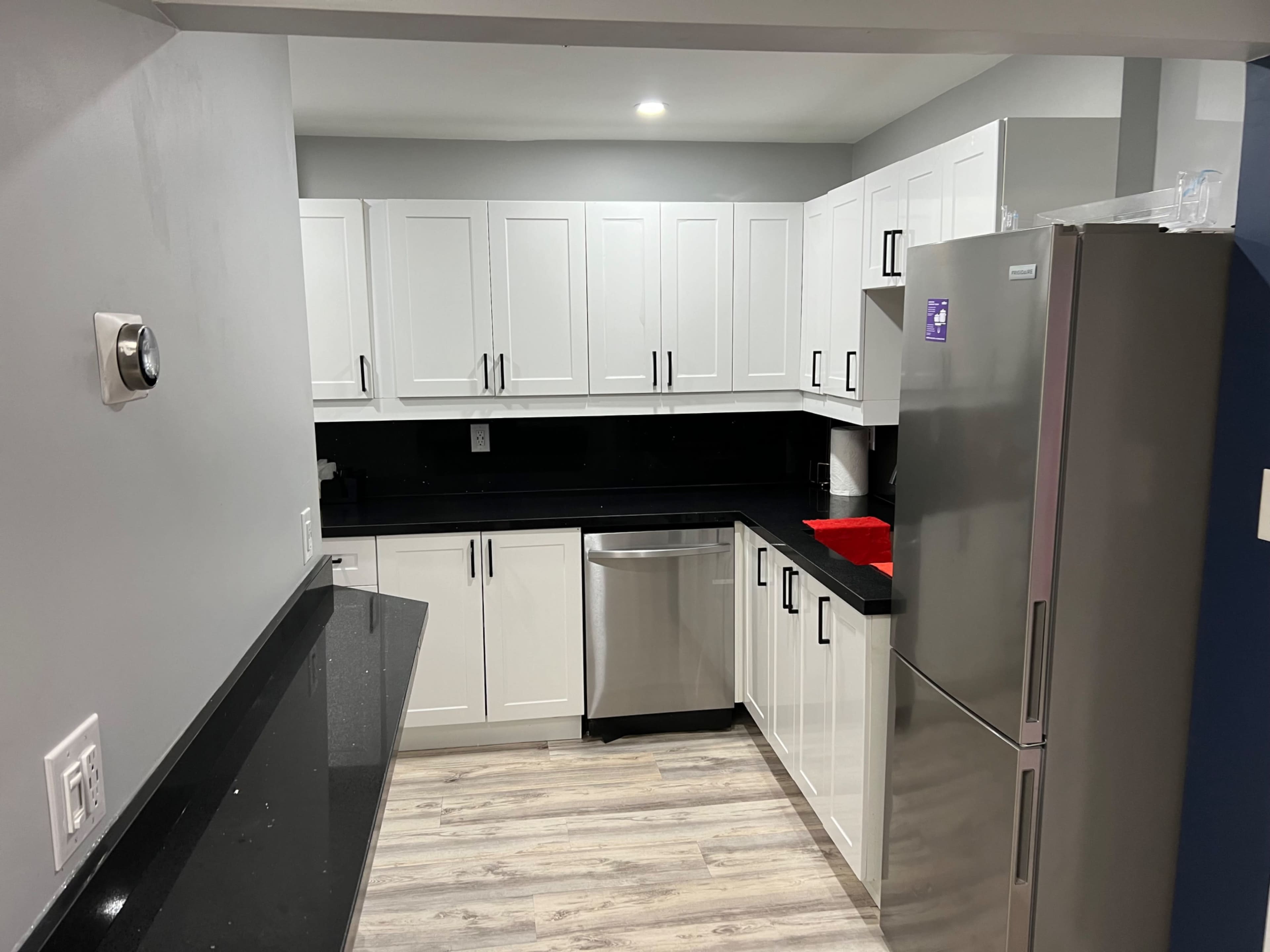 A modern kitchen featuring white cabinetry, a stainless steel refrigerator, and black countertops.