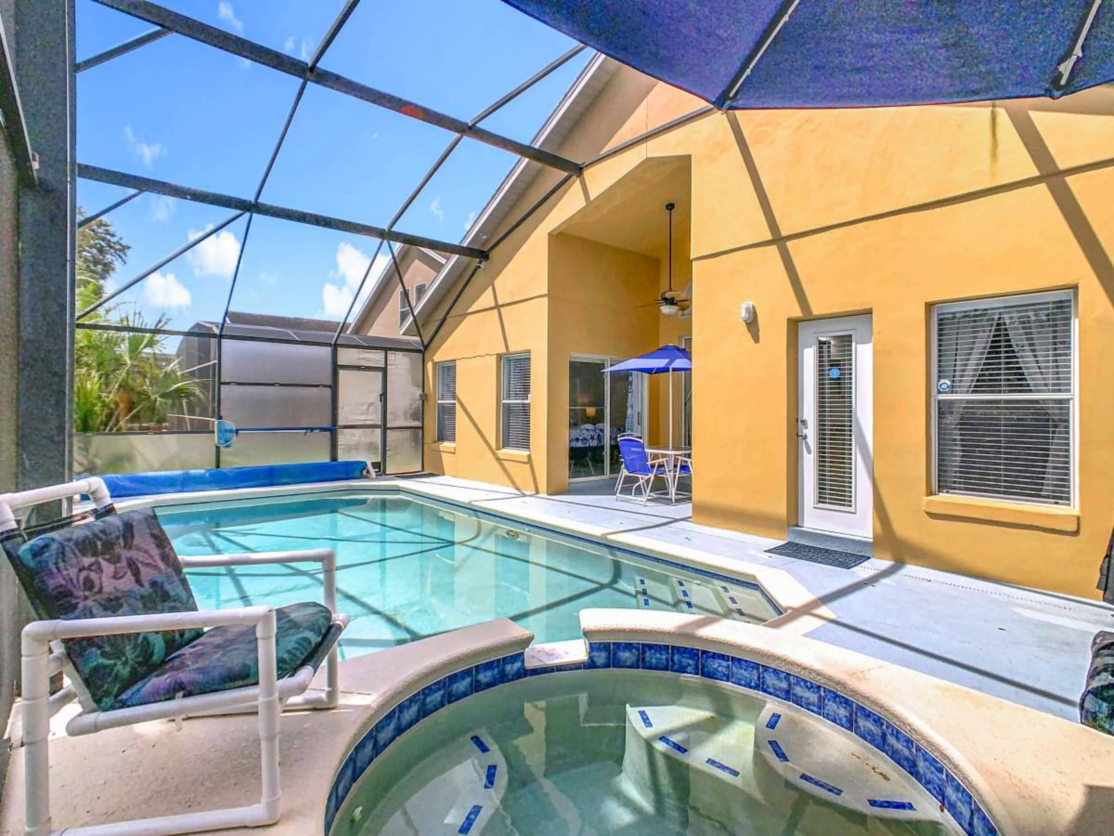 The image shows an indoor pool area with a hot tub and seating, surrounded by a screened enclosure and bright yellow walls.