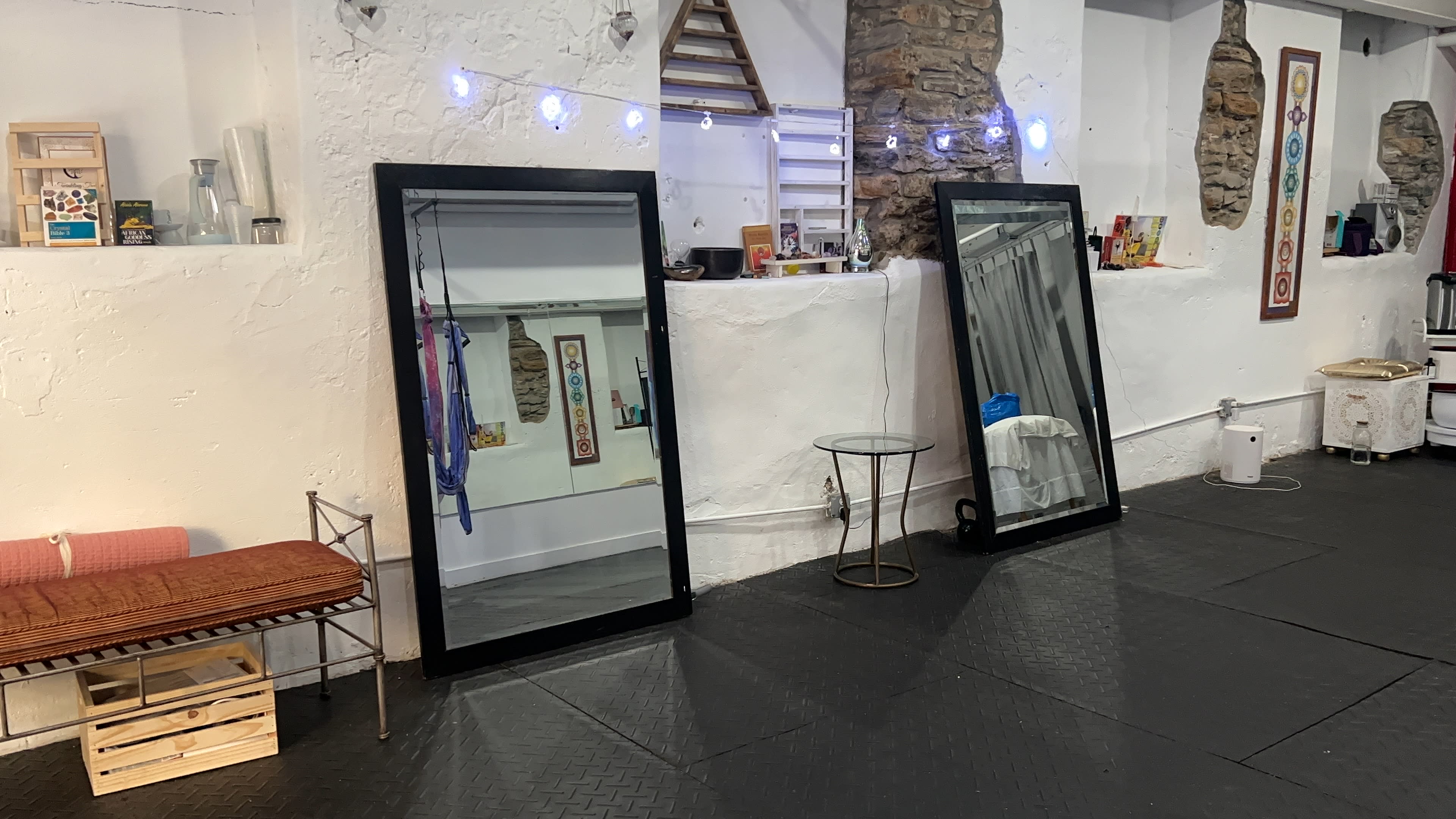 A room with two large mirrors positioned against a white wall, alongside a small side table and a wooden bench.
