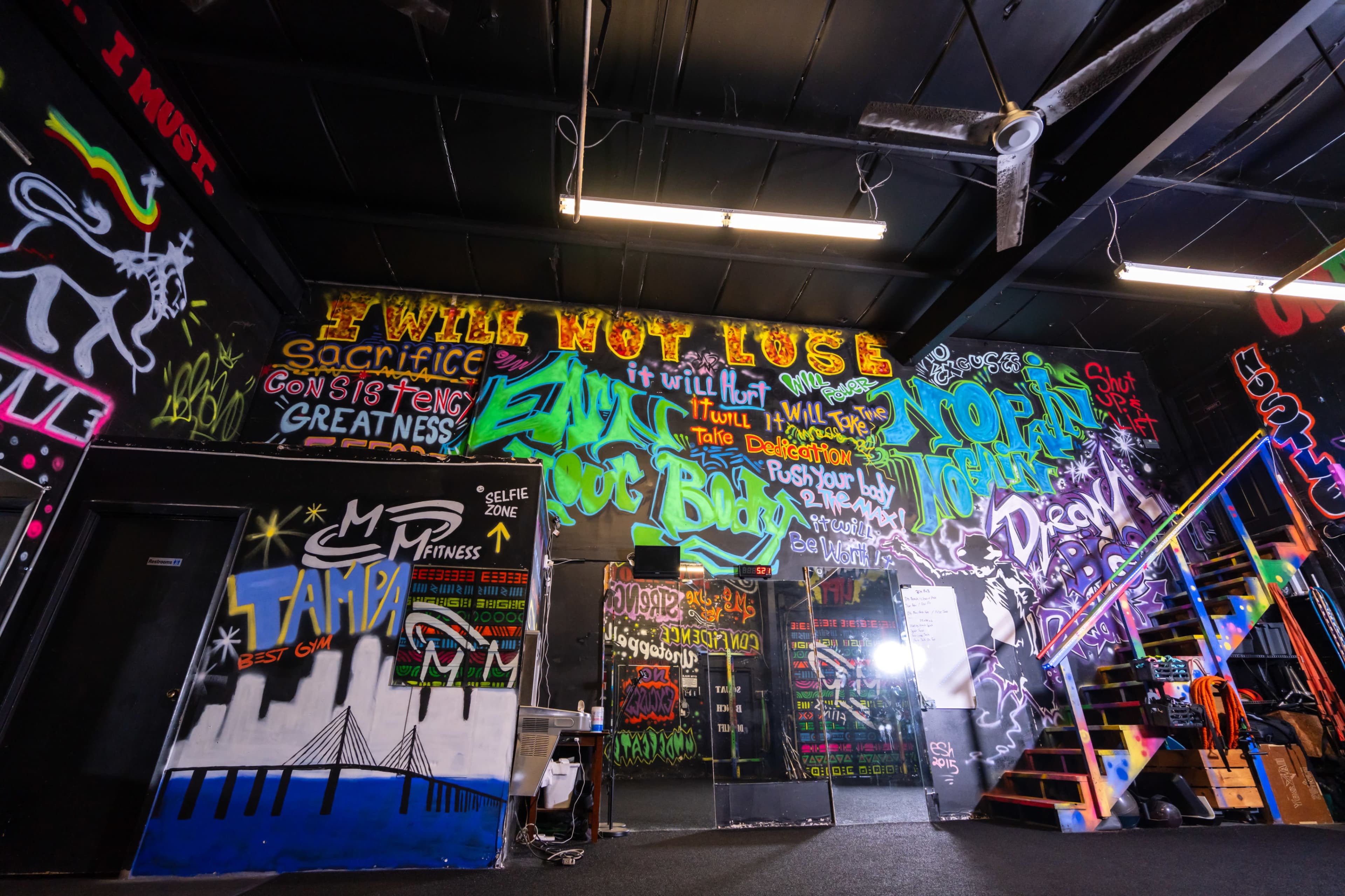 A gym interior featuring colorful graffiti on the walls with motivational phrases and artwork.