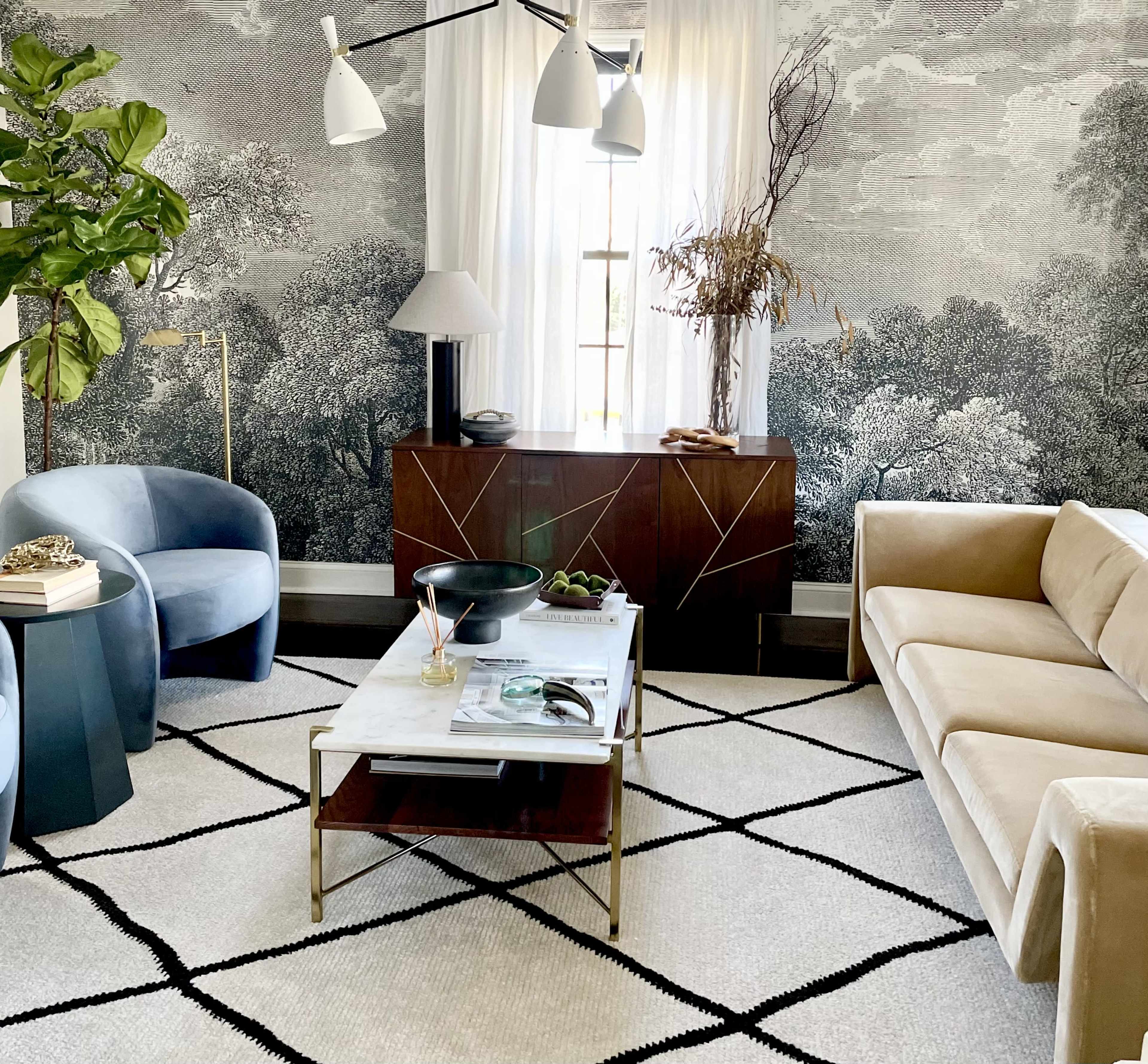A modern living room with a light-colored sofa, a coffee table, and a large, patterned wall mural featuring trees and foliage.