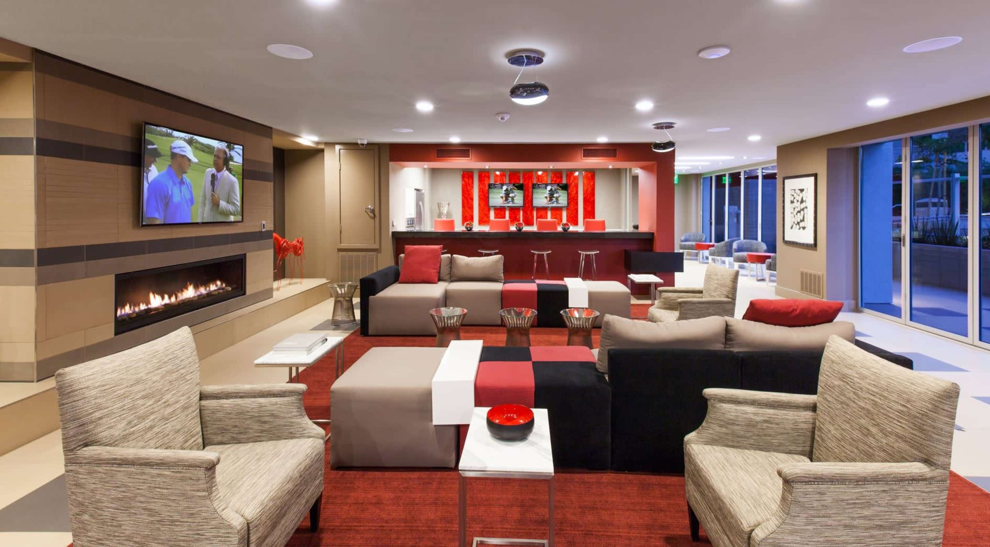 The modern lounge area features comfortable seating arrangements, a flat-screen TV, and a bar with high stools, all set against a backdrop of contemporary decor.