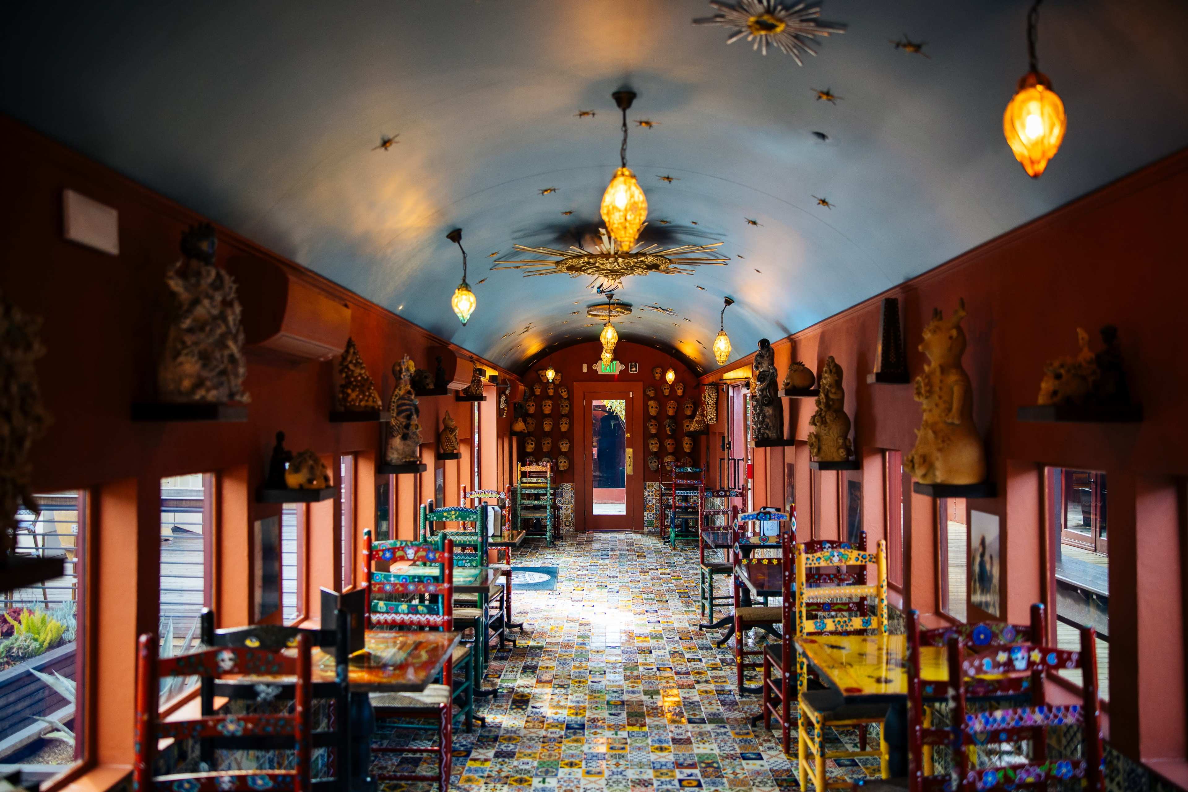 The image shows a colorful dining area with decorative chairs and walls adorned with sculptures and artistic decor.