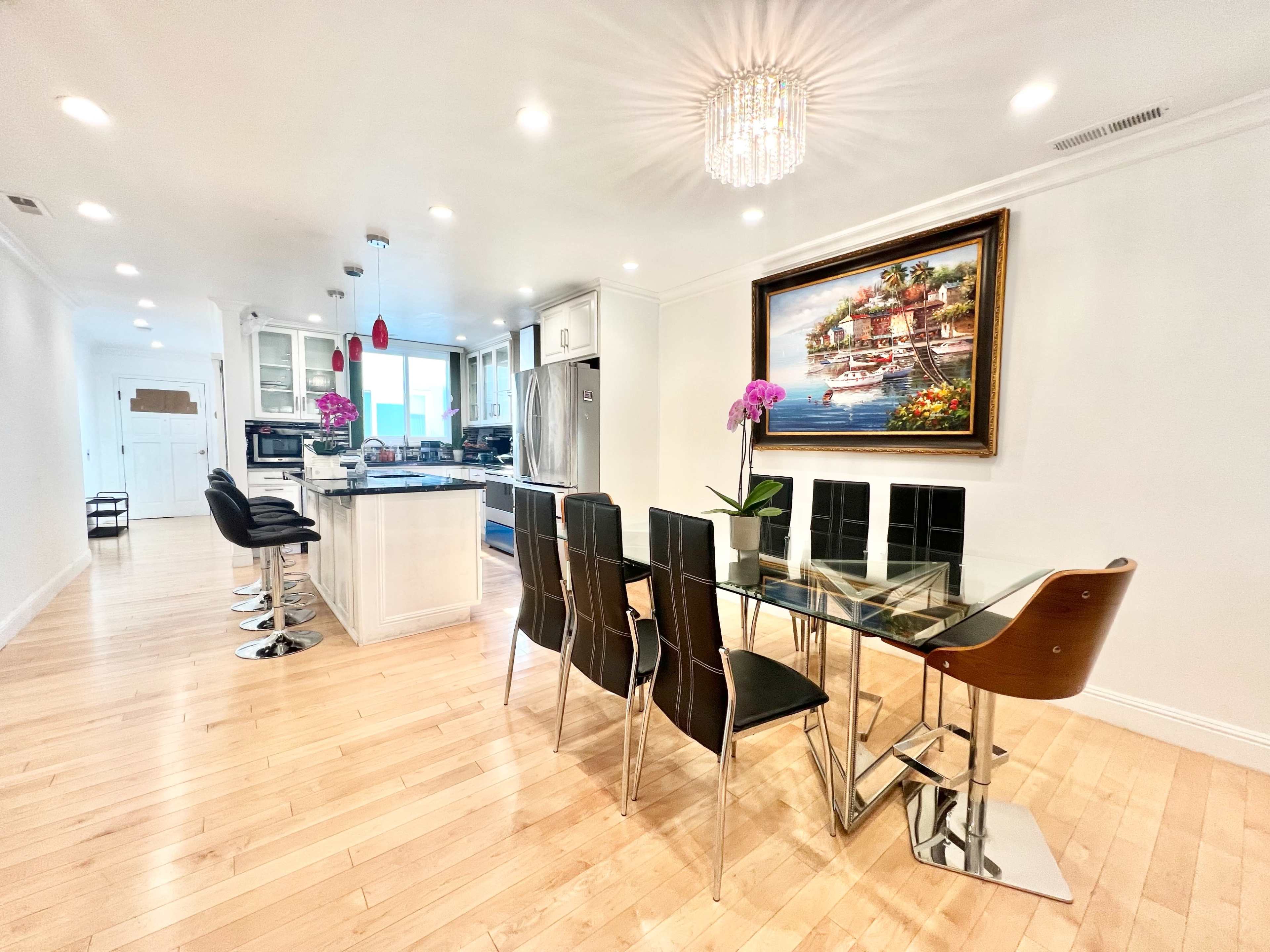 A modern kitchen and dining area featuring a glass dining table with black chairs and a contemporary chandelier.