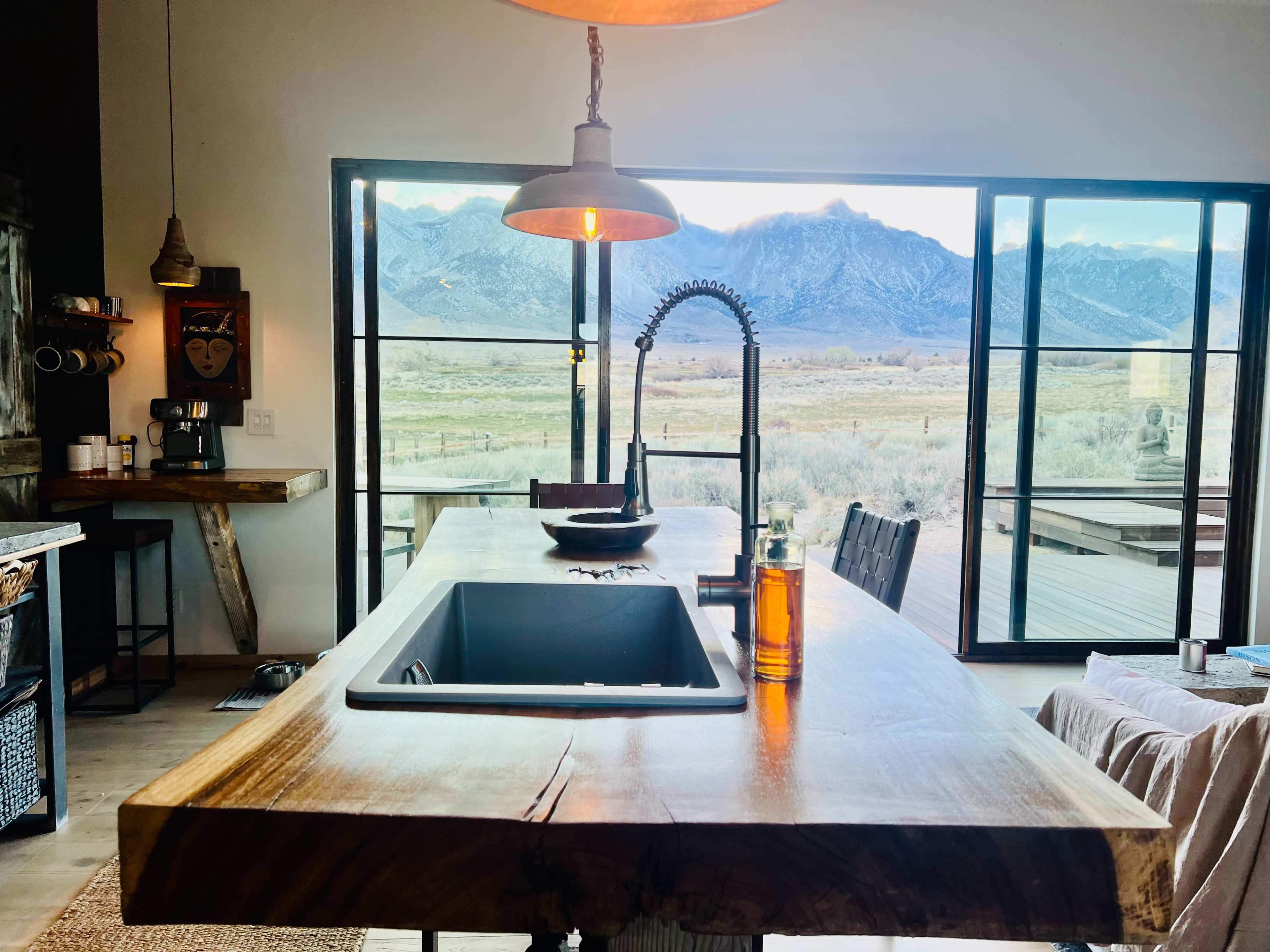 A spacious kitchen features a wooden island with a sink, surrounded by windows showcasing a mountainous landscape.