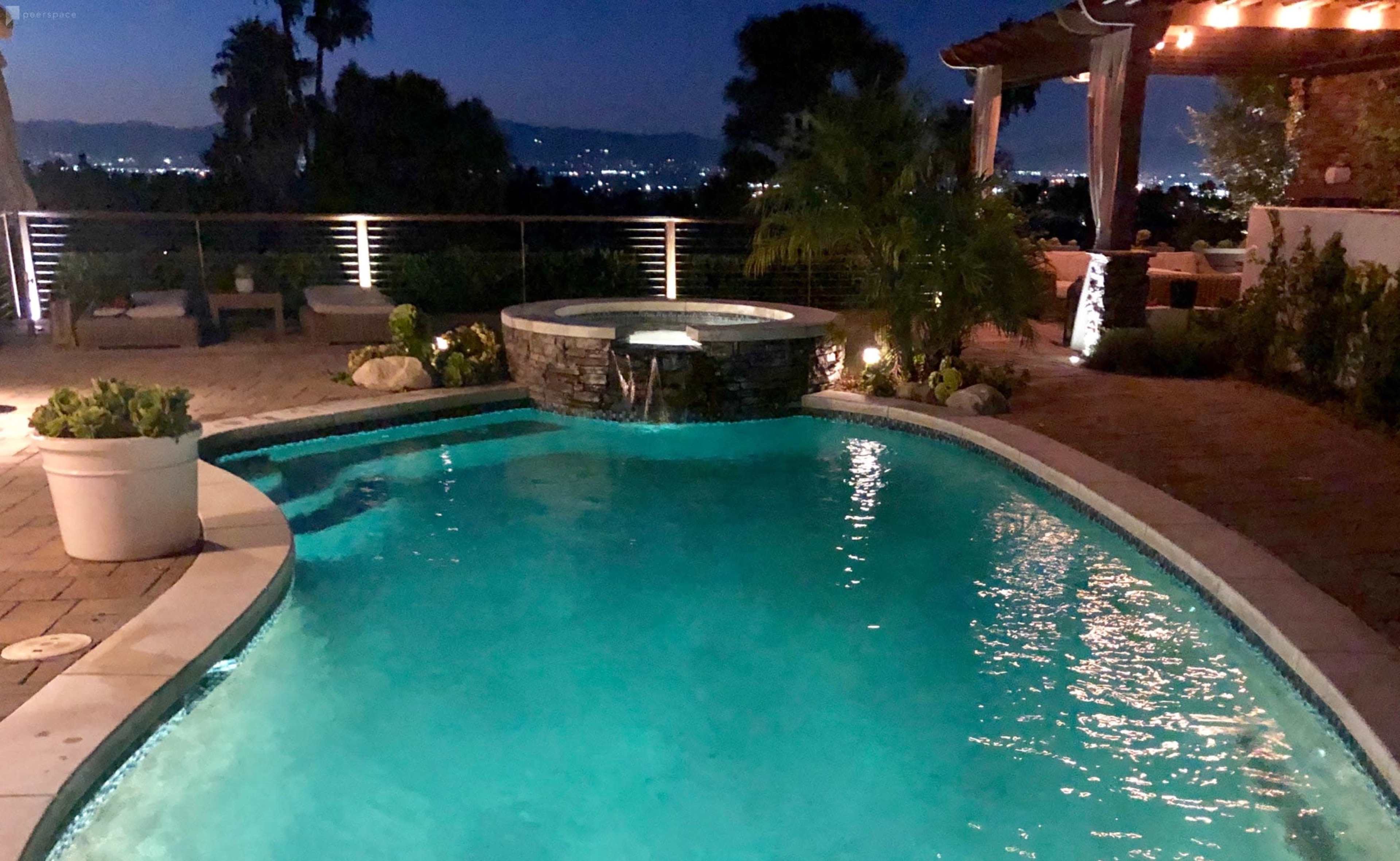 A well-lit swimming pool with a spa and landscaped surroundings is visible at night.