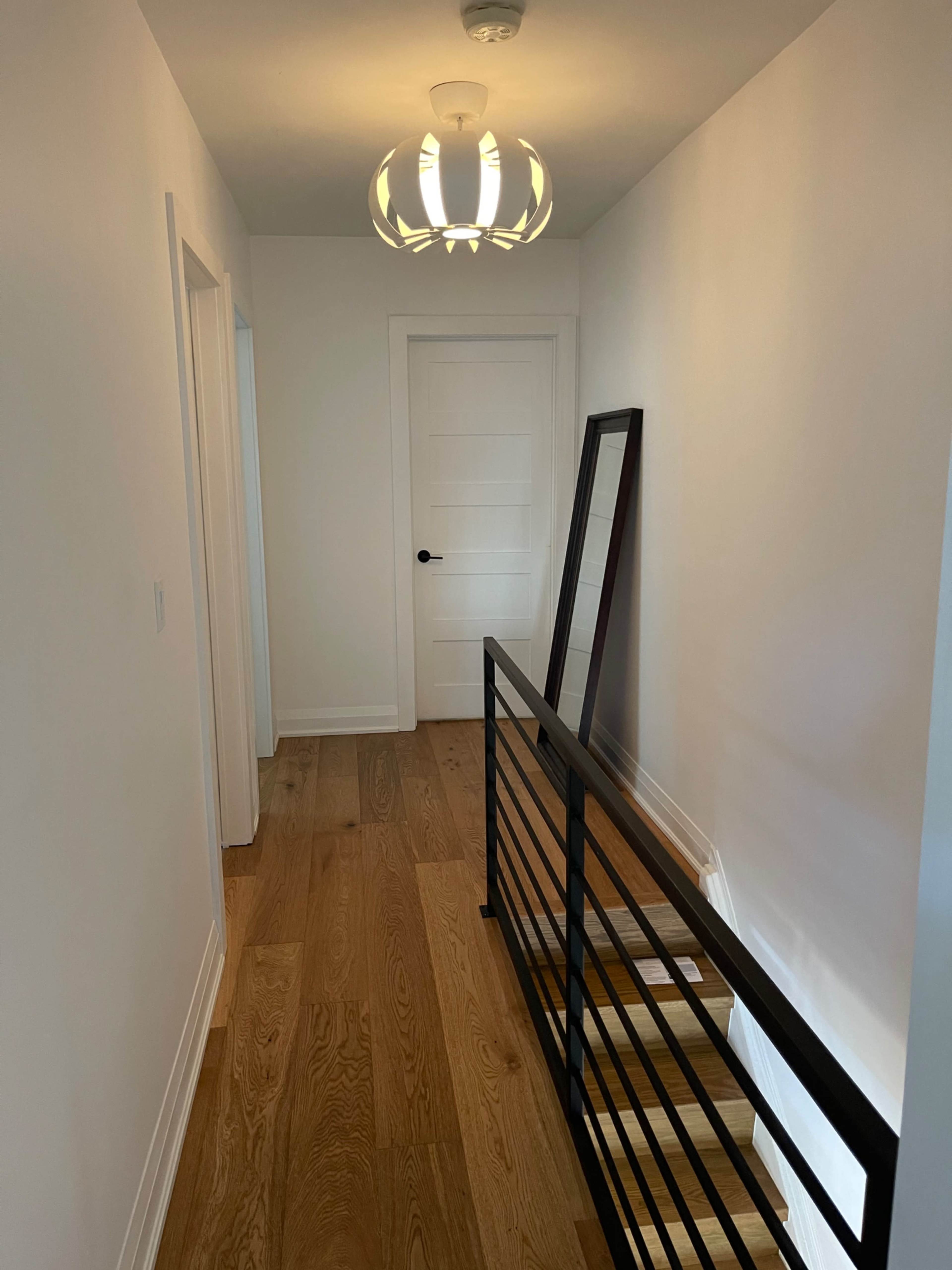 A sleek hallway featuring a wooden floor, a mirror mounted against the wall, and a modern light fixture hanging from the ceiling.