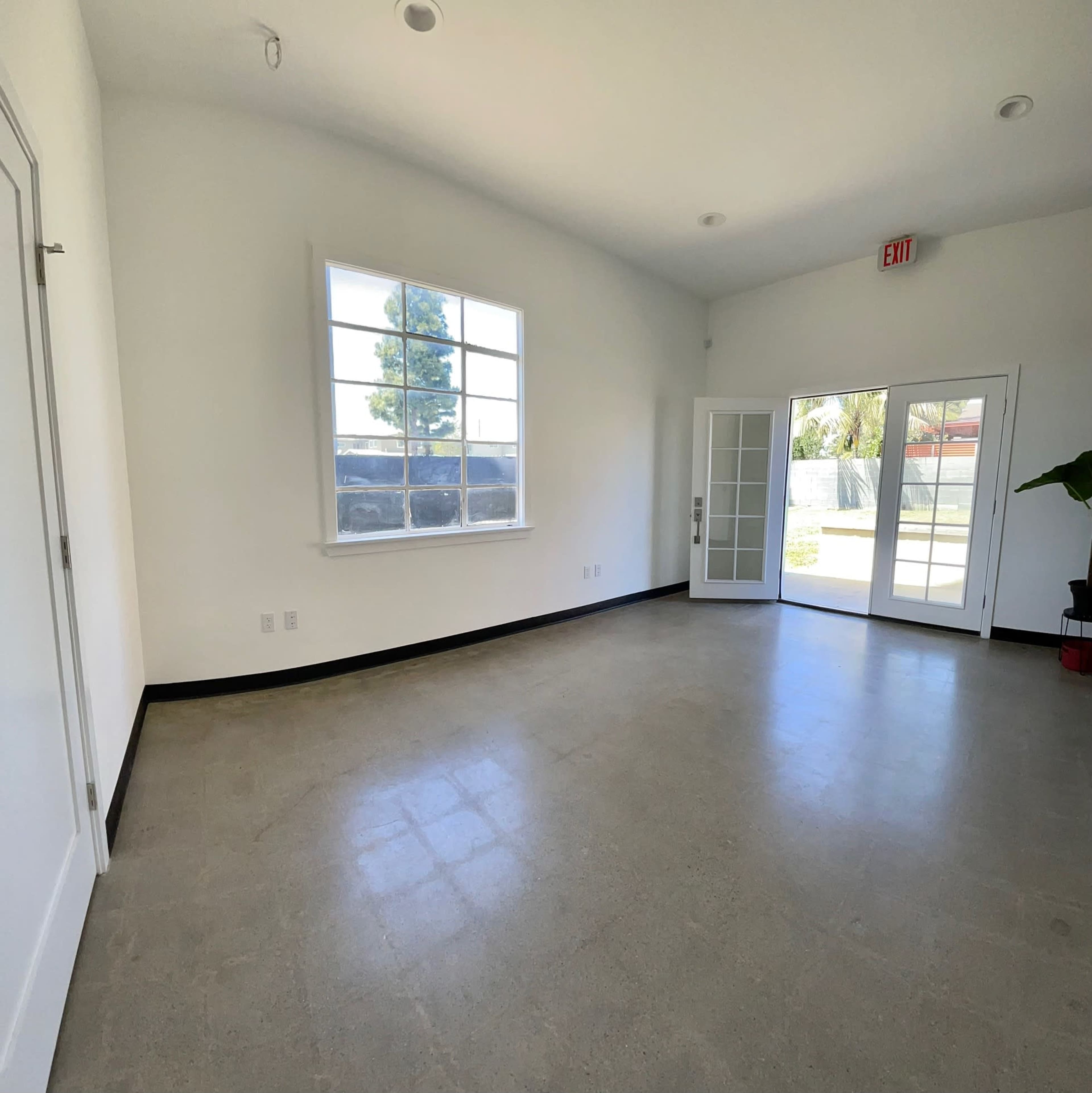 An empty room with a large window and double doors leading to an outdoor area.