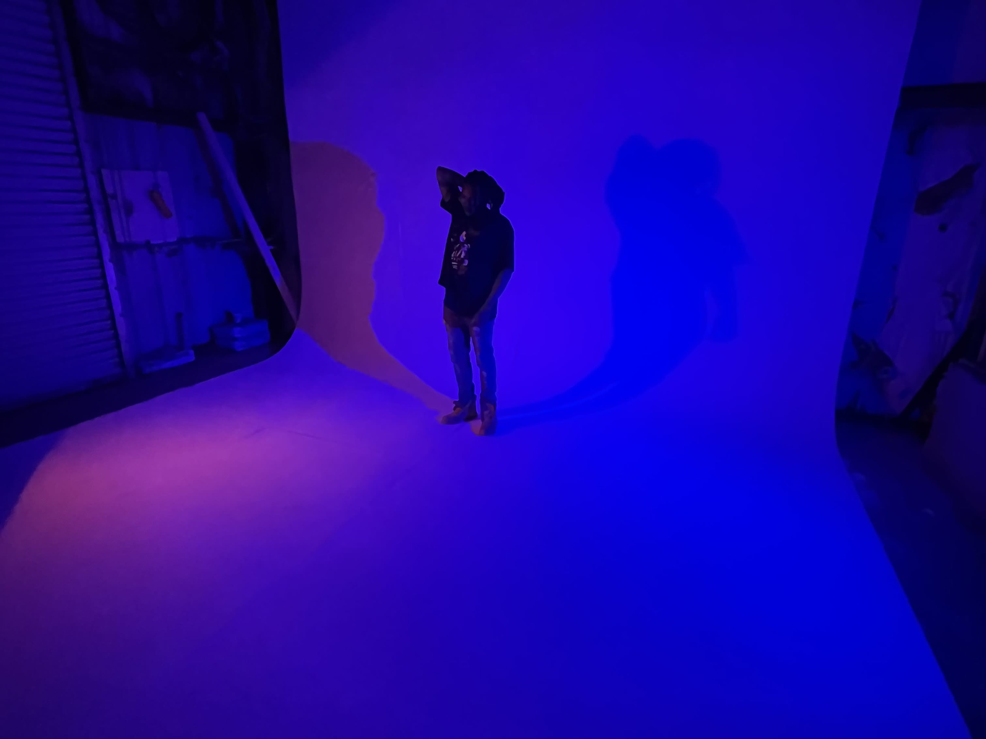 A person stands in front of a large curved backdrop illuminated with blue light, casting long shadows on the floor.