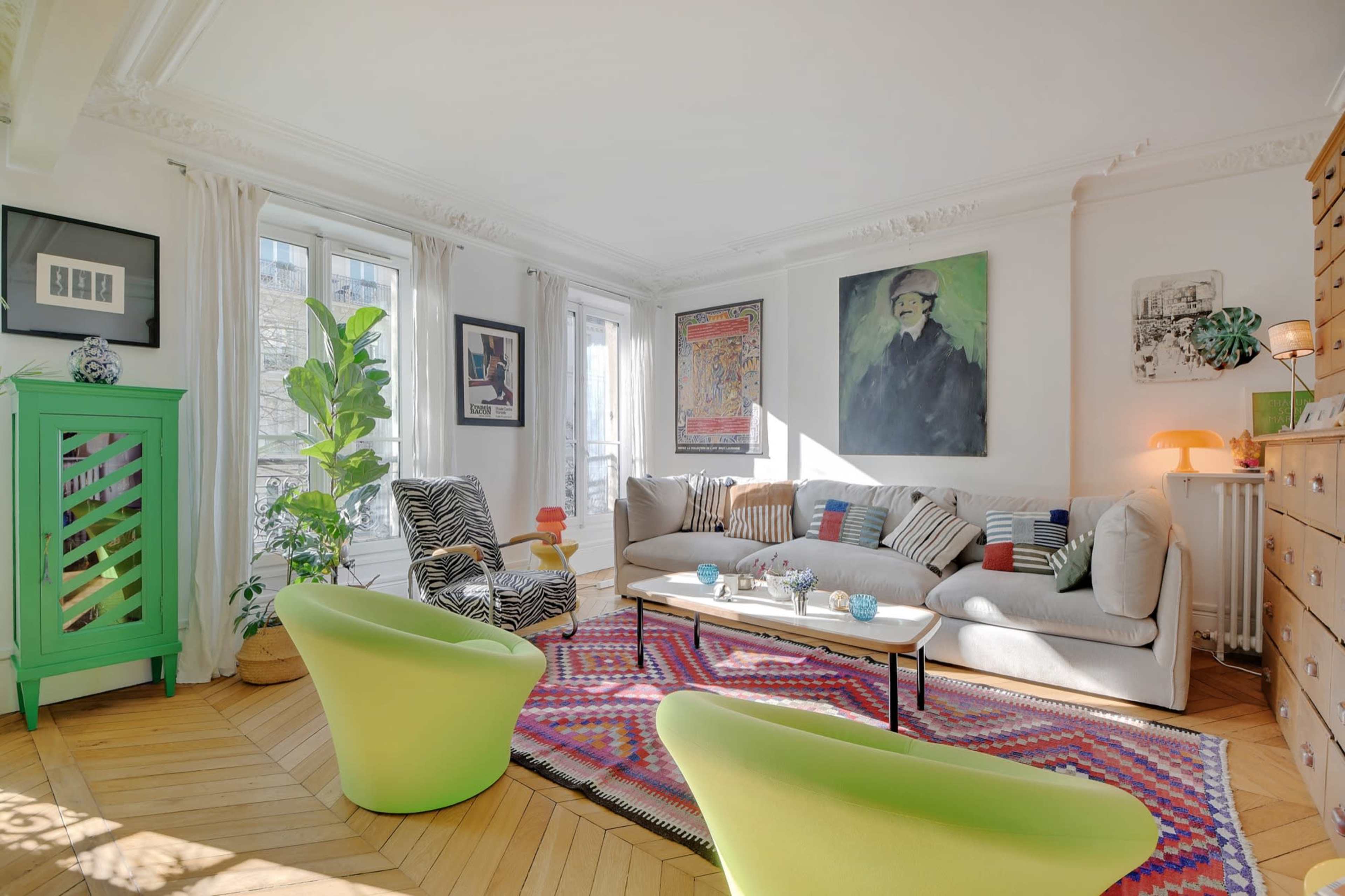 A bright living room features a mix of contemporary furniture, colorful rugs, and large windows that allow ample natural light.