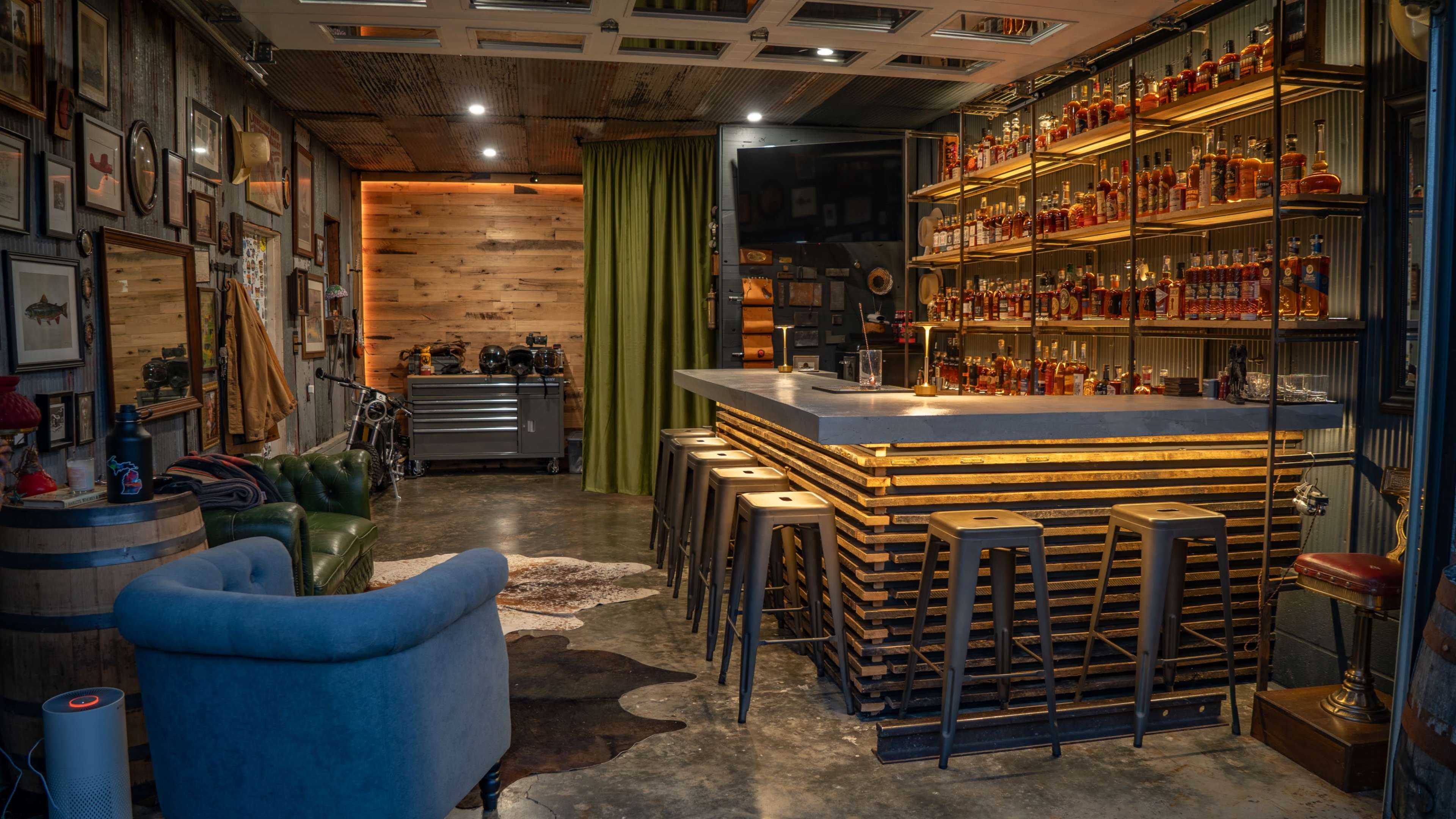 The image showcases a stylish bar area with a light-colored countertop, shelves lined with bottles, and seating arranged around it, complemented by decorative elements on the walls and a green curtain.