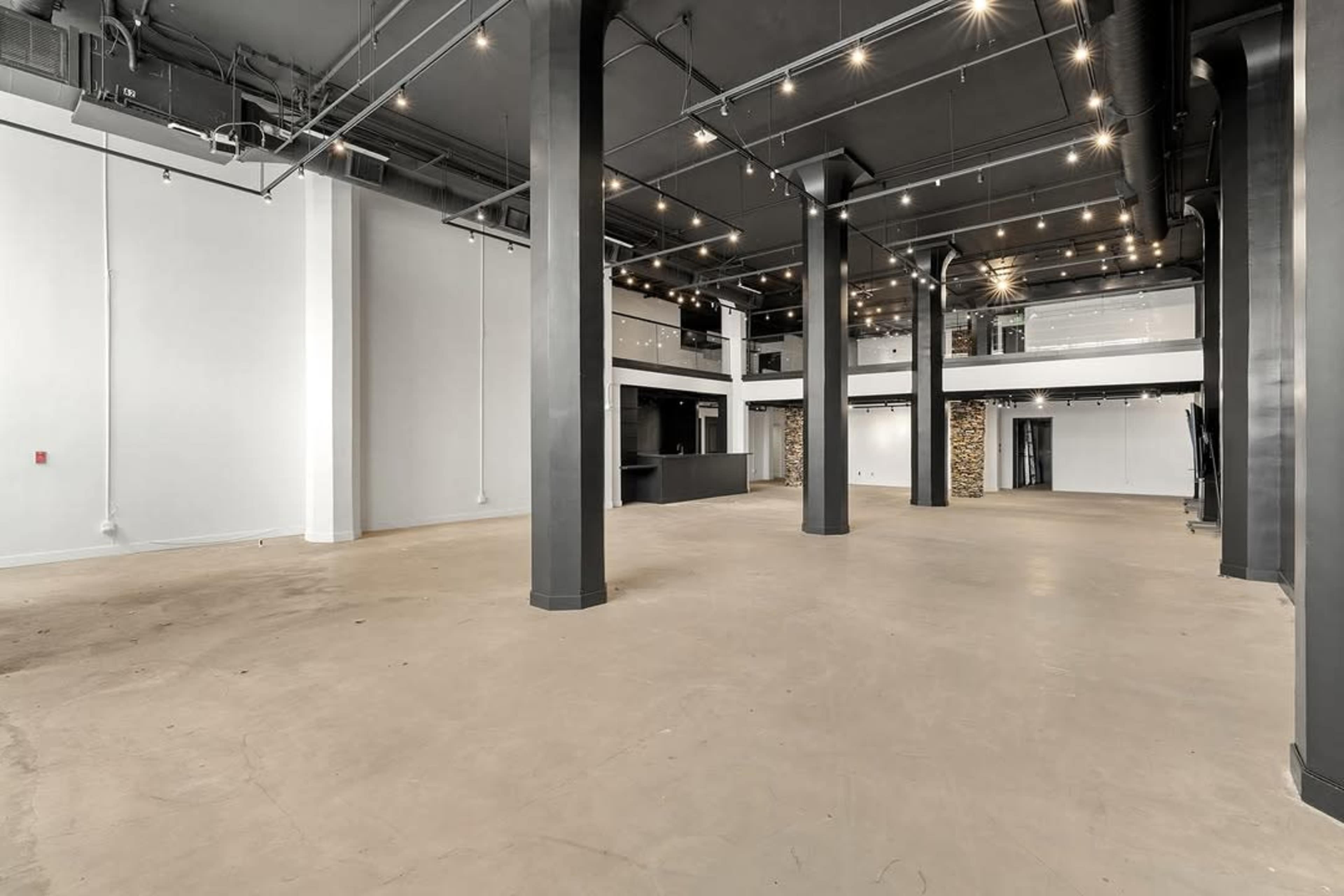 The image shows a spacious, empty commercial interior with high ceilings, exposed columns, and large windows.
