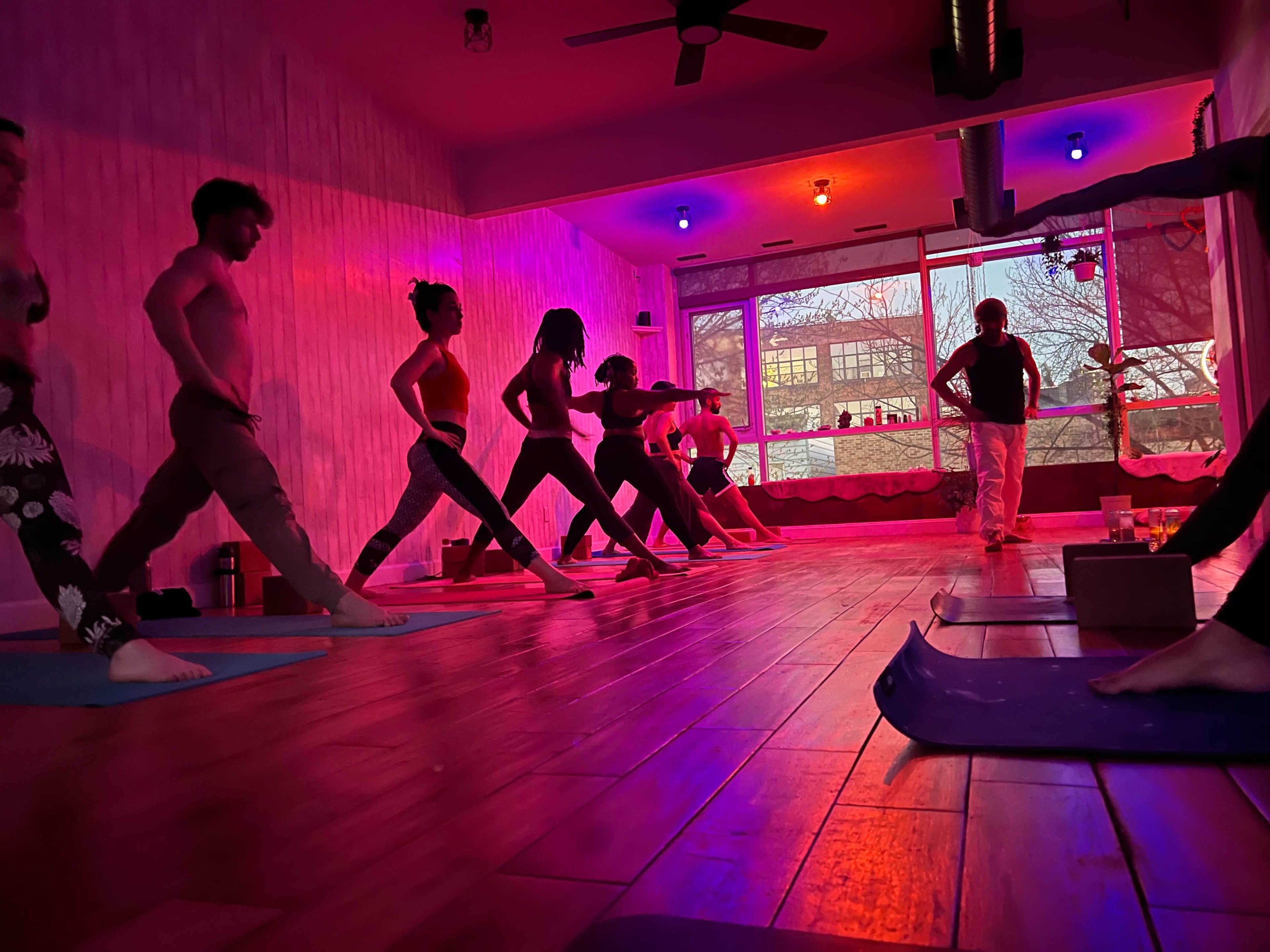 A group of individuals practices yoga in a studio with colorful lighting.