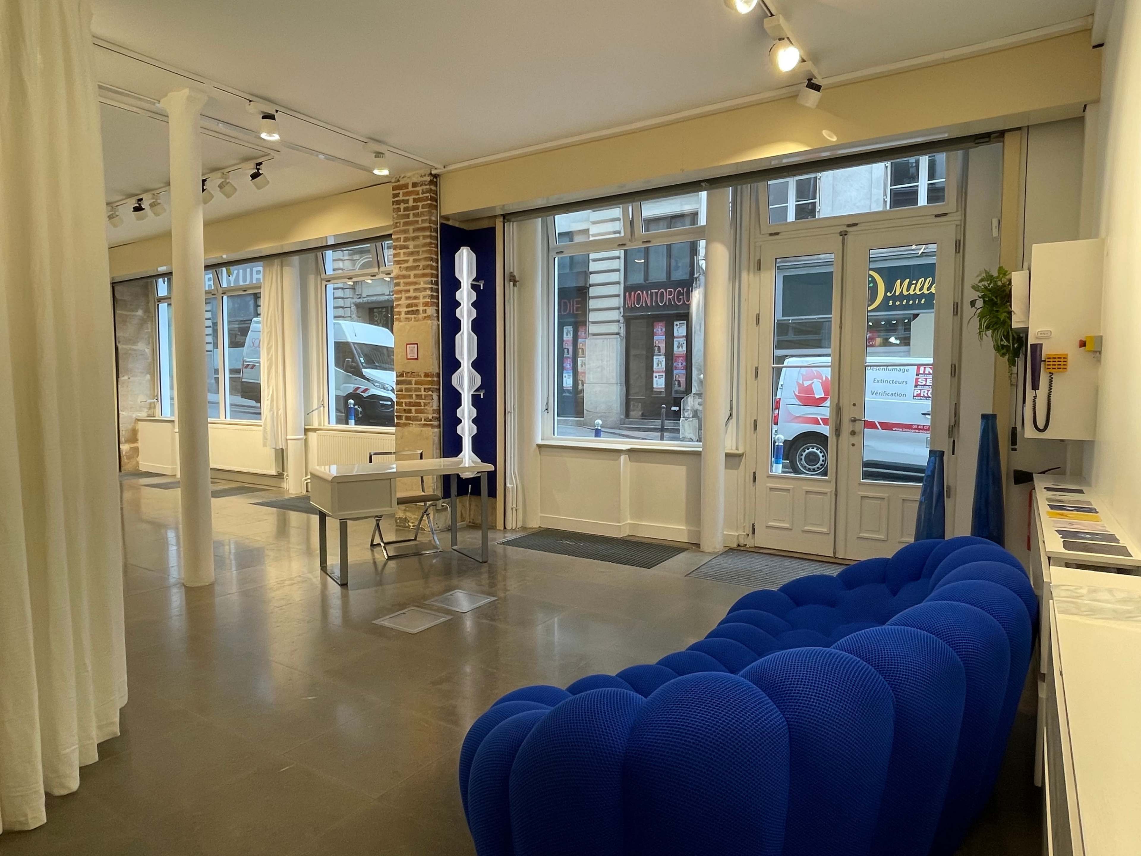A modern interior space featuring a blue sofa, a small table, and large windows allowing natural light to enter.