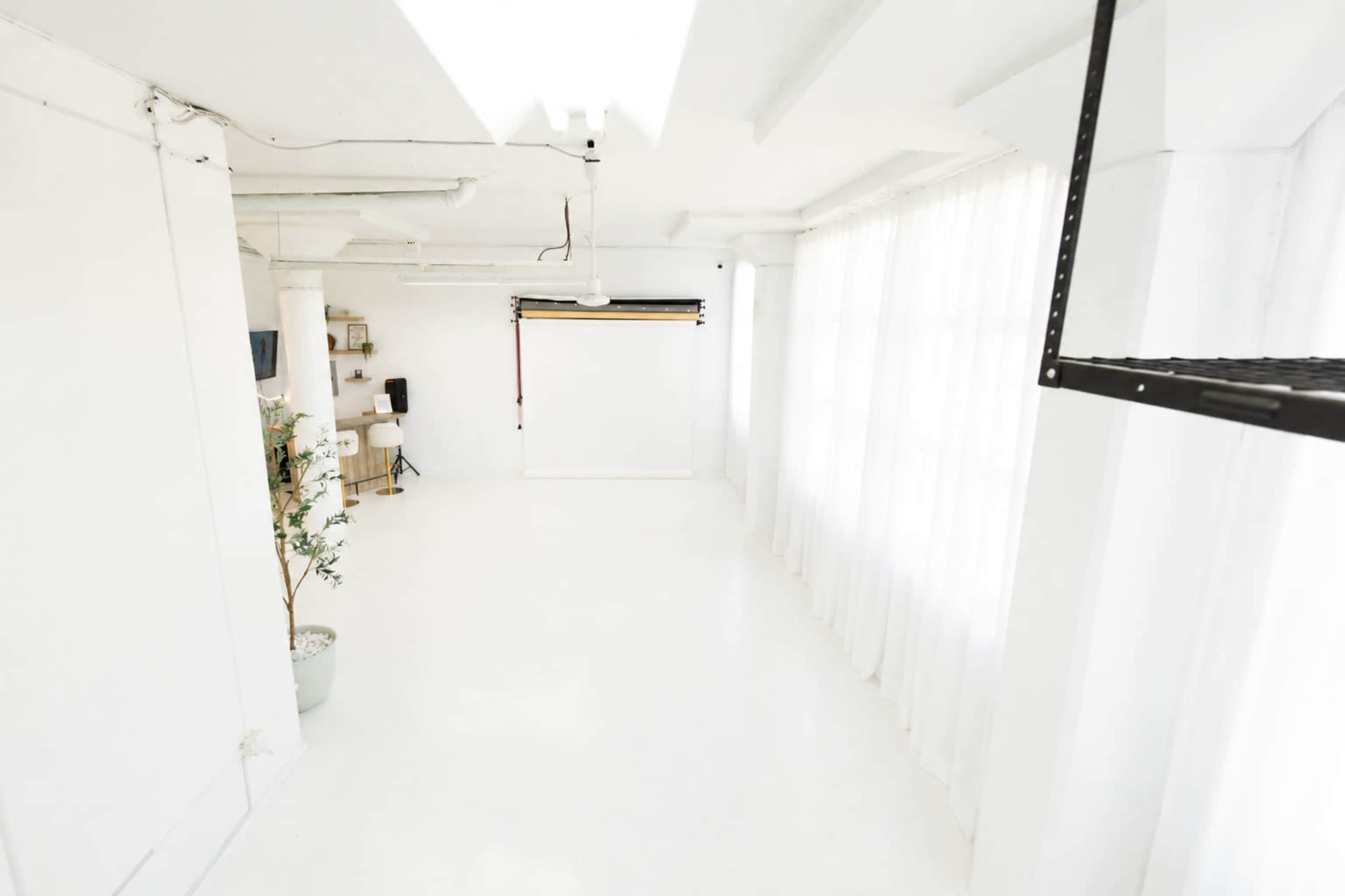 The image shows a bright, spacious studio with white walls, large windows, and a minimalistic setup.