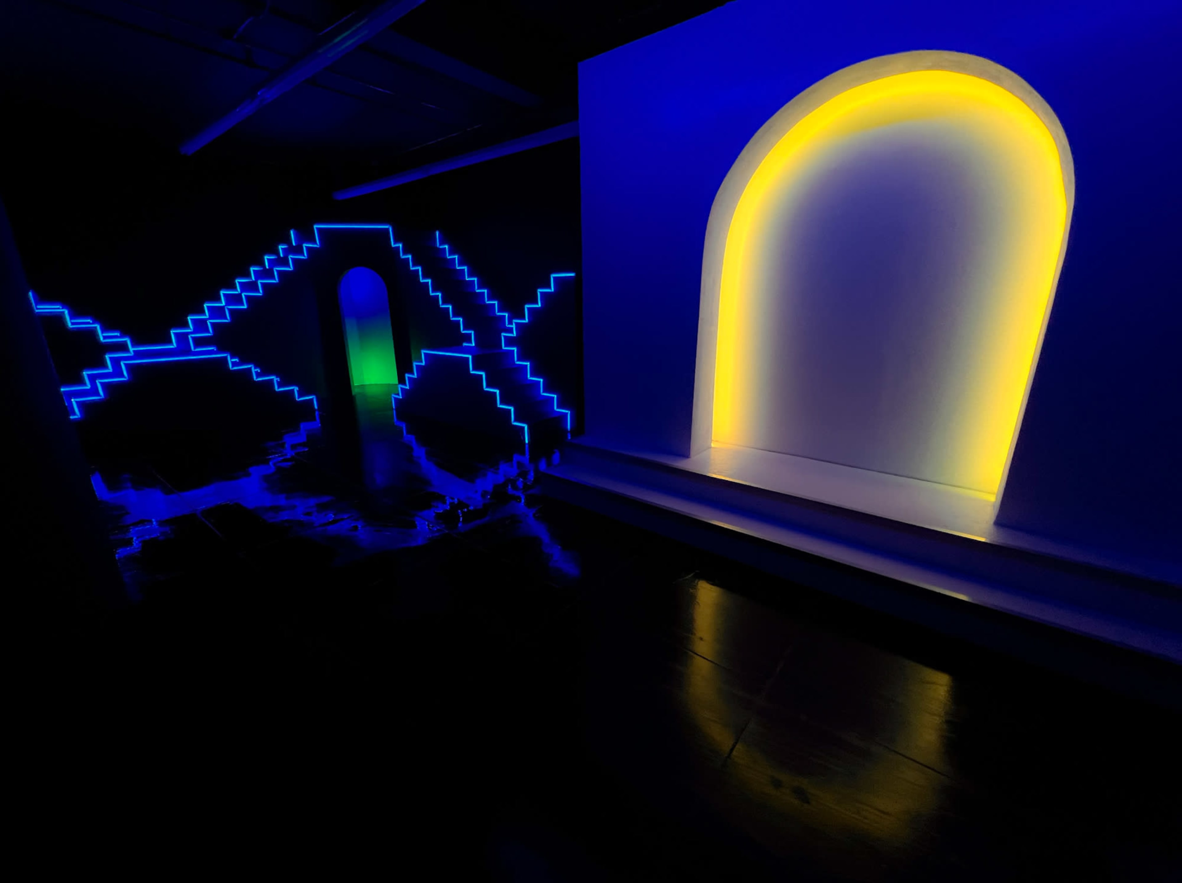 A dark room illuminated by blue and yellow LED lights, with geometric patterns and two illuminated archways.