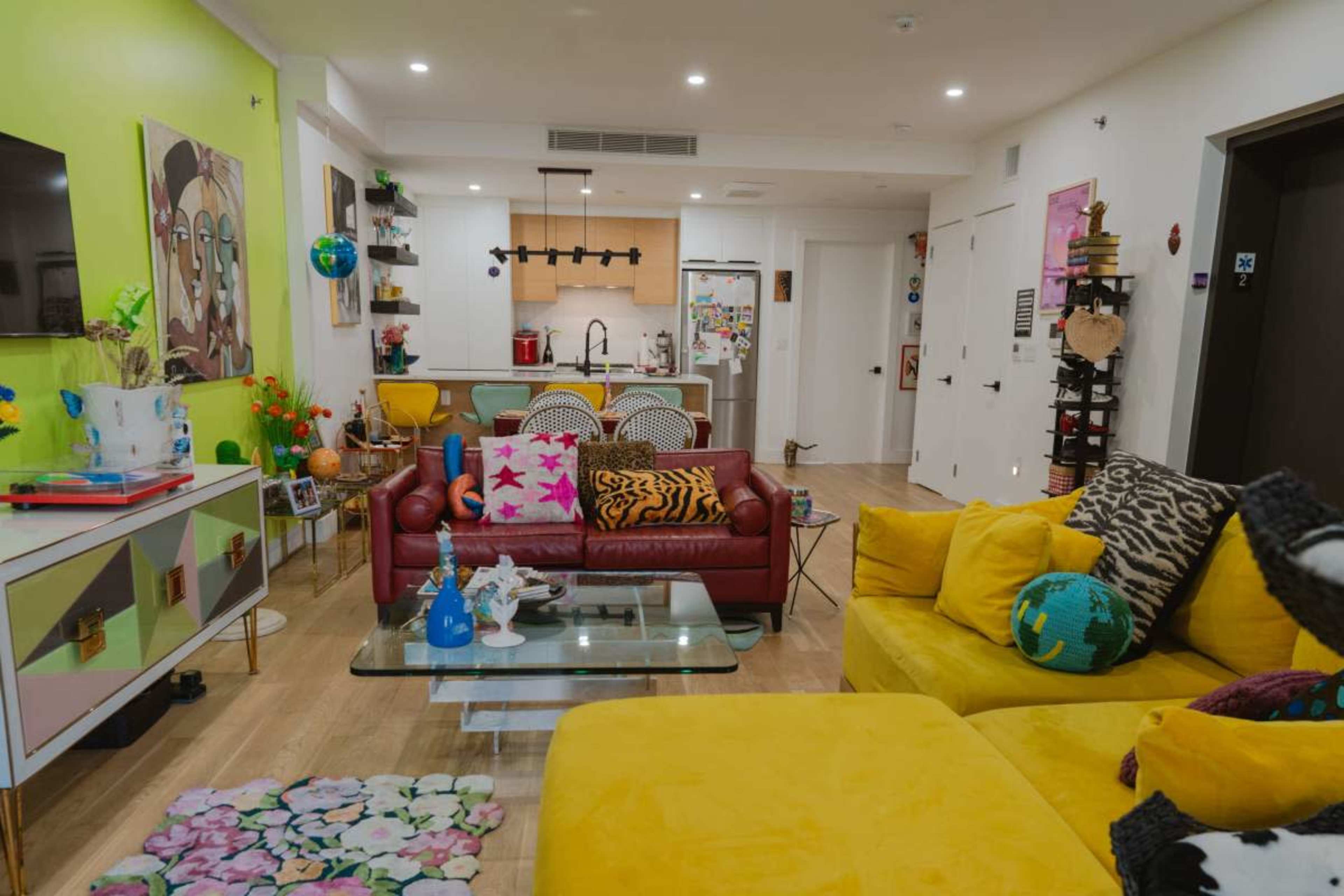 A bright living area with a mix of colorful furniture, including a yellow sofa and a red couch, adjacent to a kitchen with modern appliances.