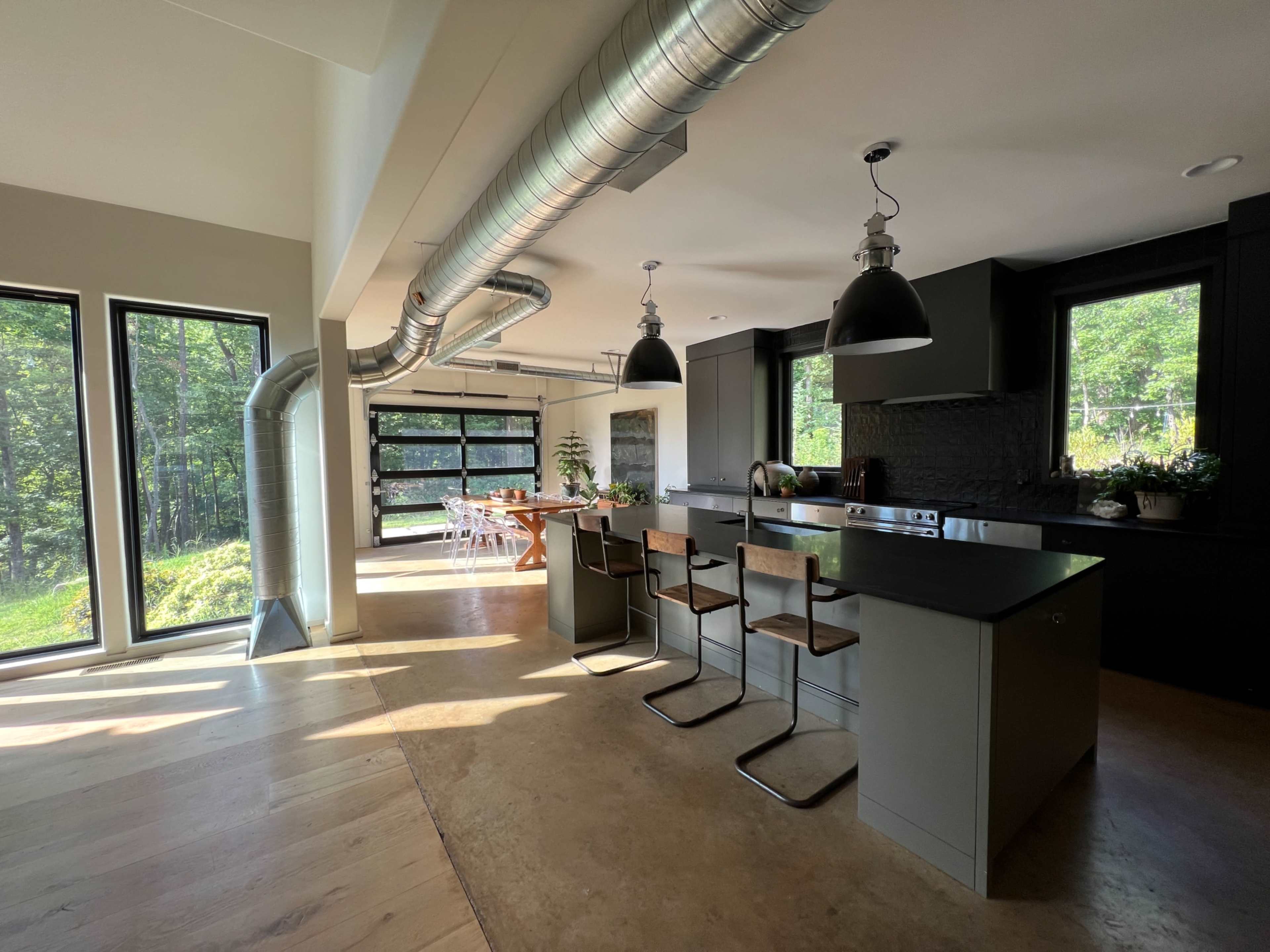 A modern kitchen features a large island with bar seating, sleek cabinetry, and expansive windows overlooking a green outdoor area.